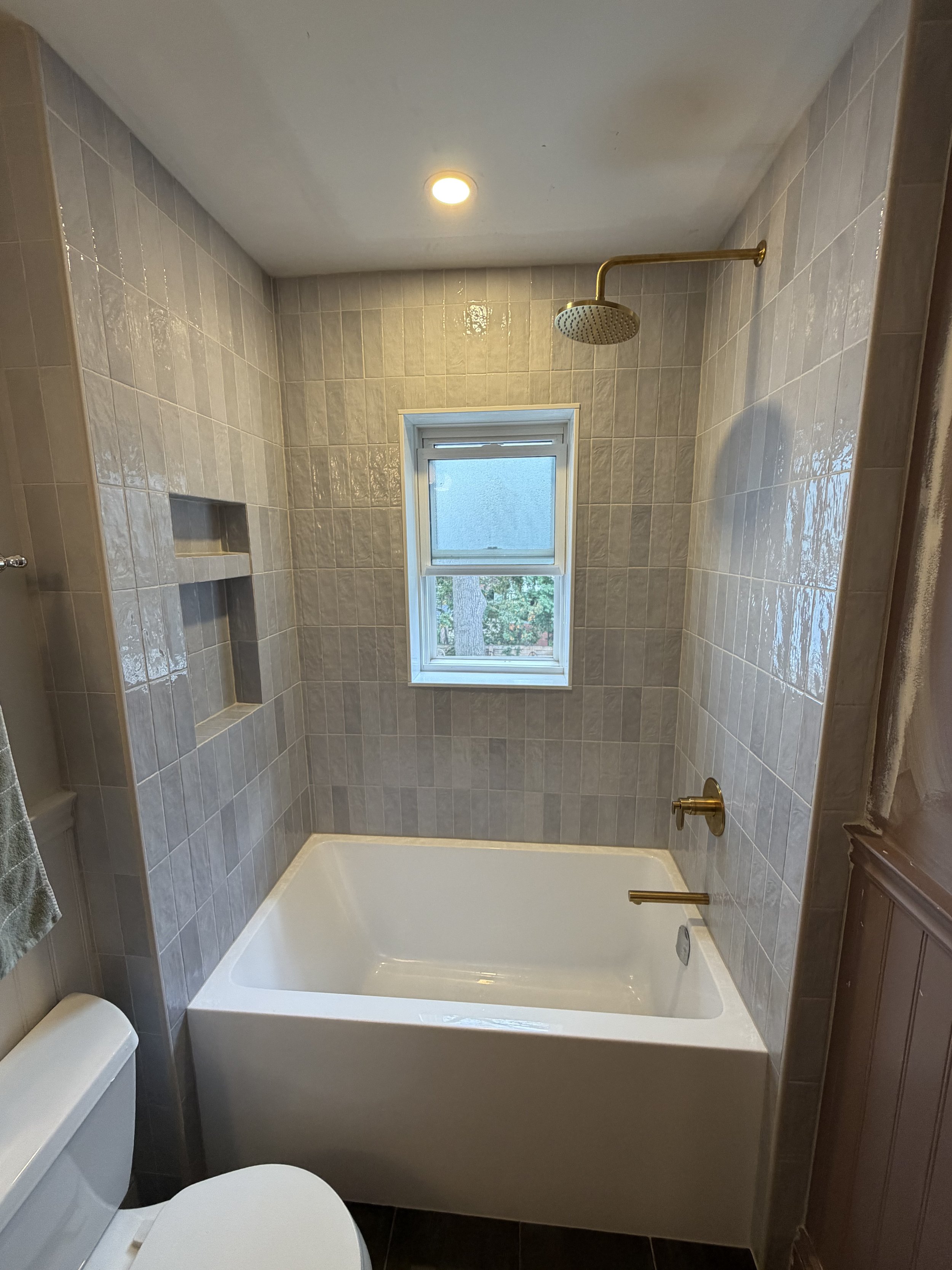 Bathroom with bathtub, window, showerhead, toilet, and beige tiled walls.