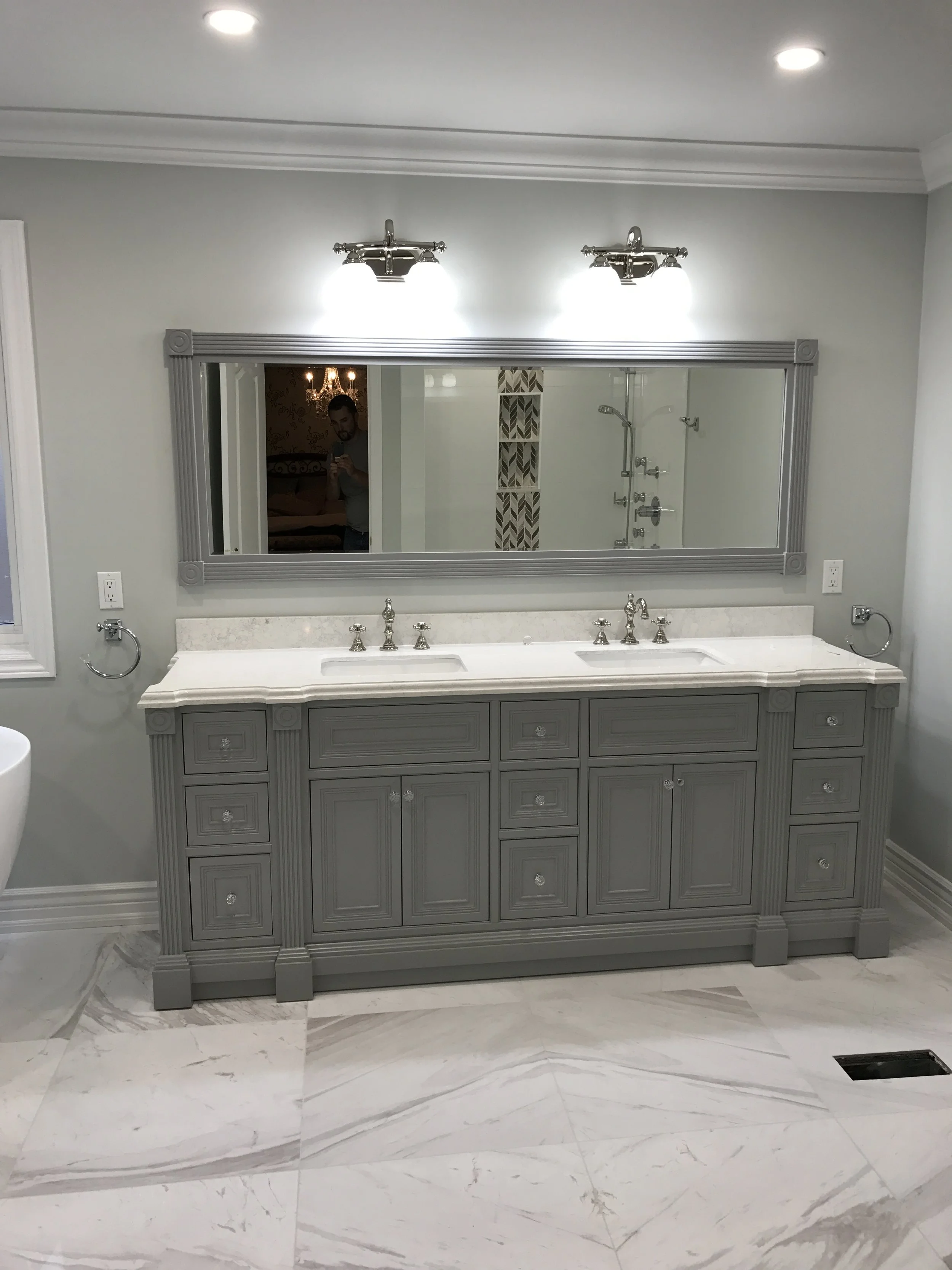 Bathroom vanity with dual sinks, large mirror, and gray cabinetry in a modern bathroom with marble flooring.