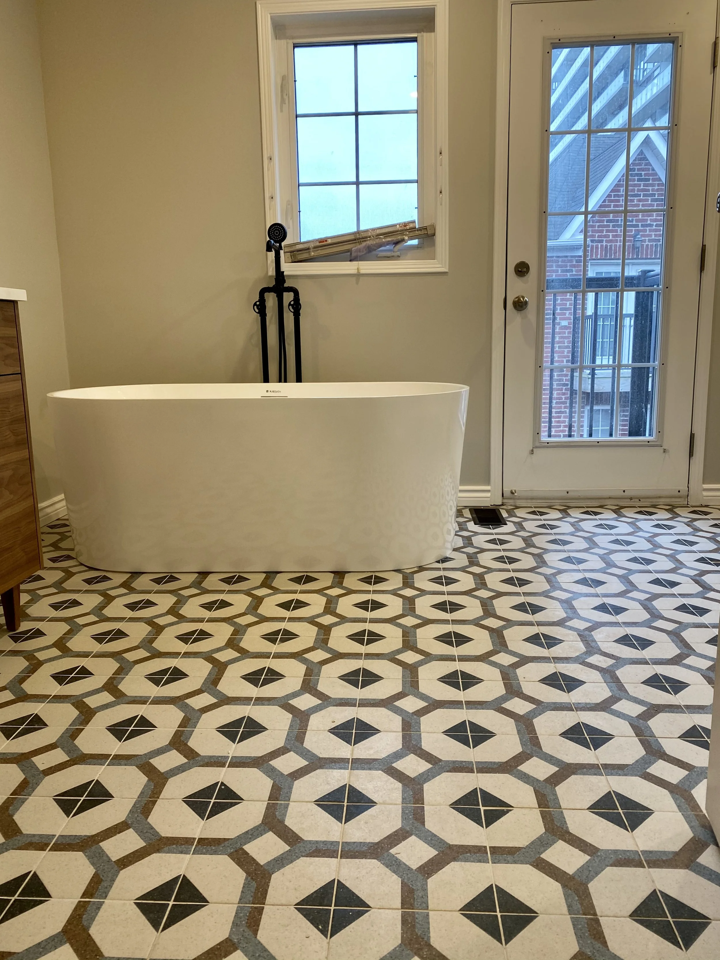A bathroom with a freestanding bathtub near a window and a door, with patterned tile flooring.
