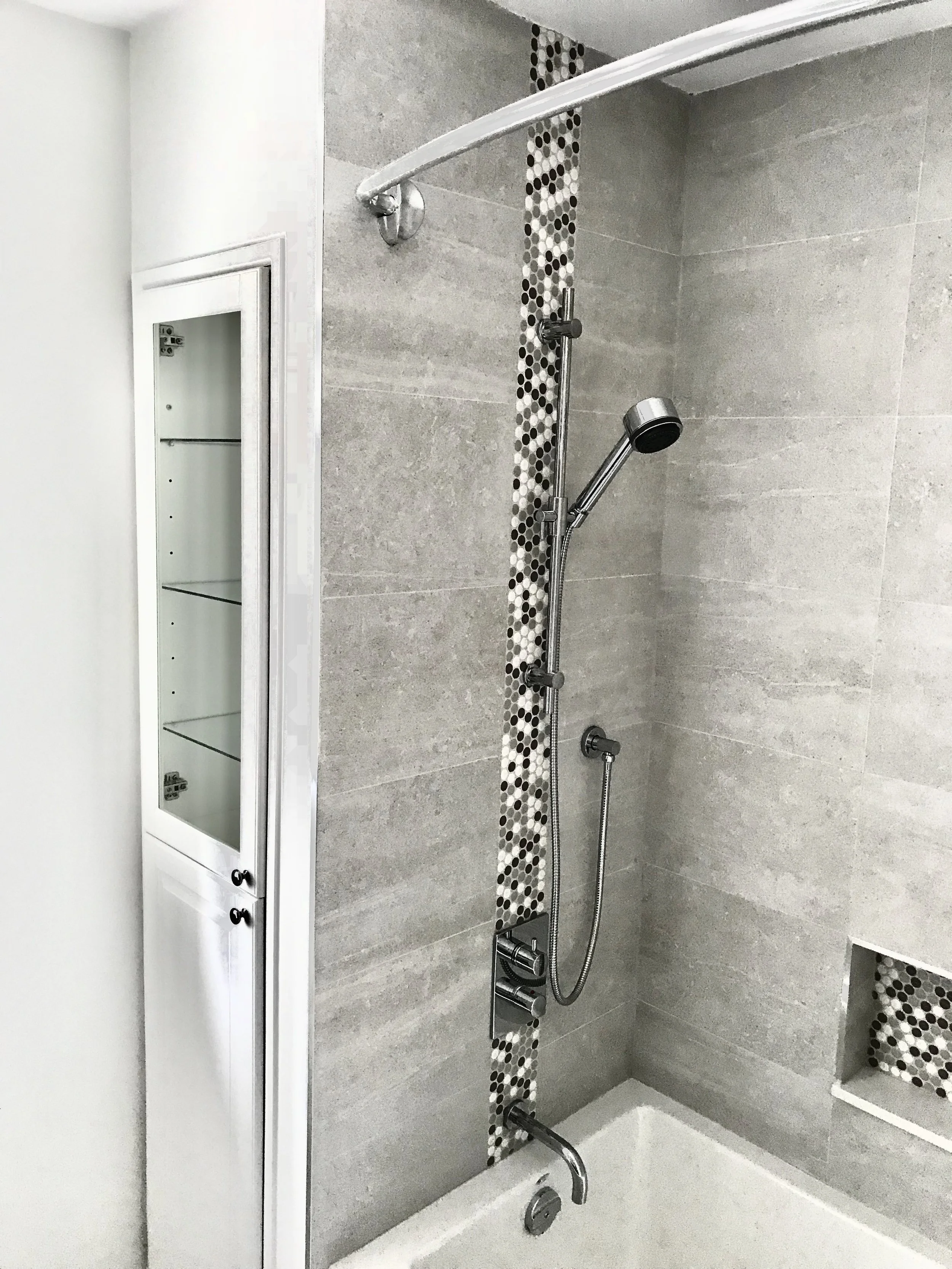 Modern shower with a handheld showerhead, a decorative vertical strip of small black, white, and gray tiles, and a built-in niche for storage.