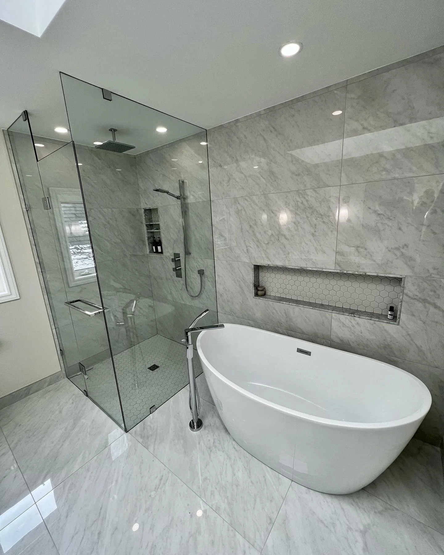 Modern bathroom with a large, white oval bathtub next to a glass-enclosed shower with marble tiles.