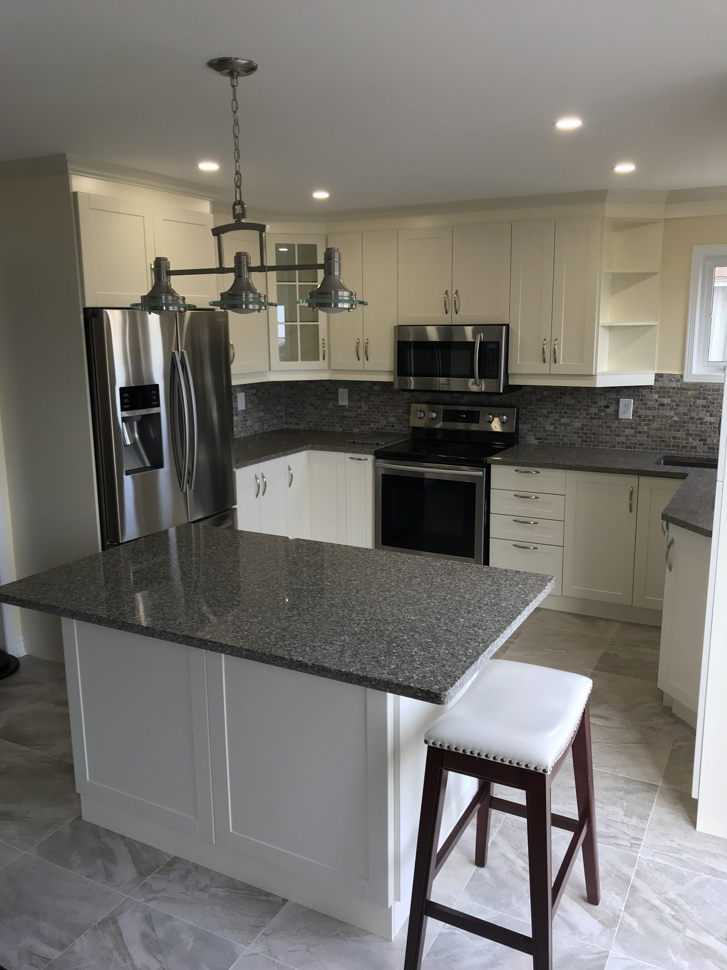 Modern kitchen with white cabinets, stainless steel appliances, granite countertops, and a small island with a bar stool.