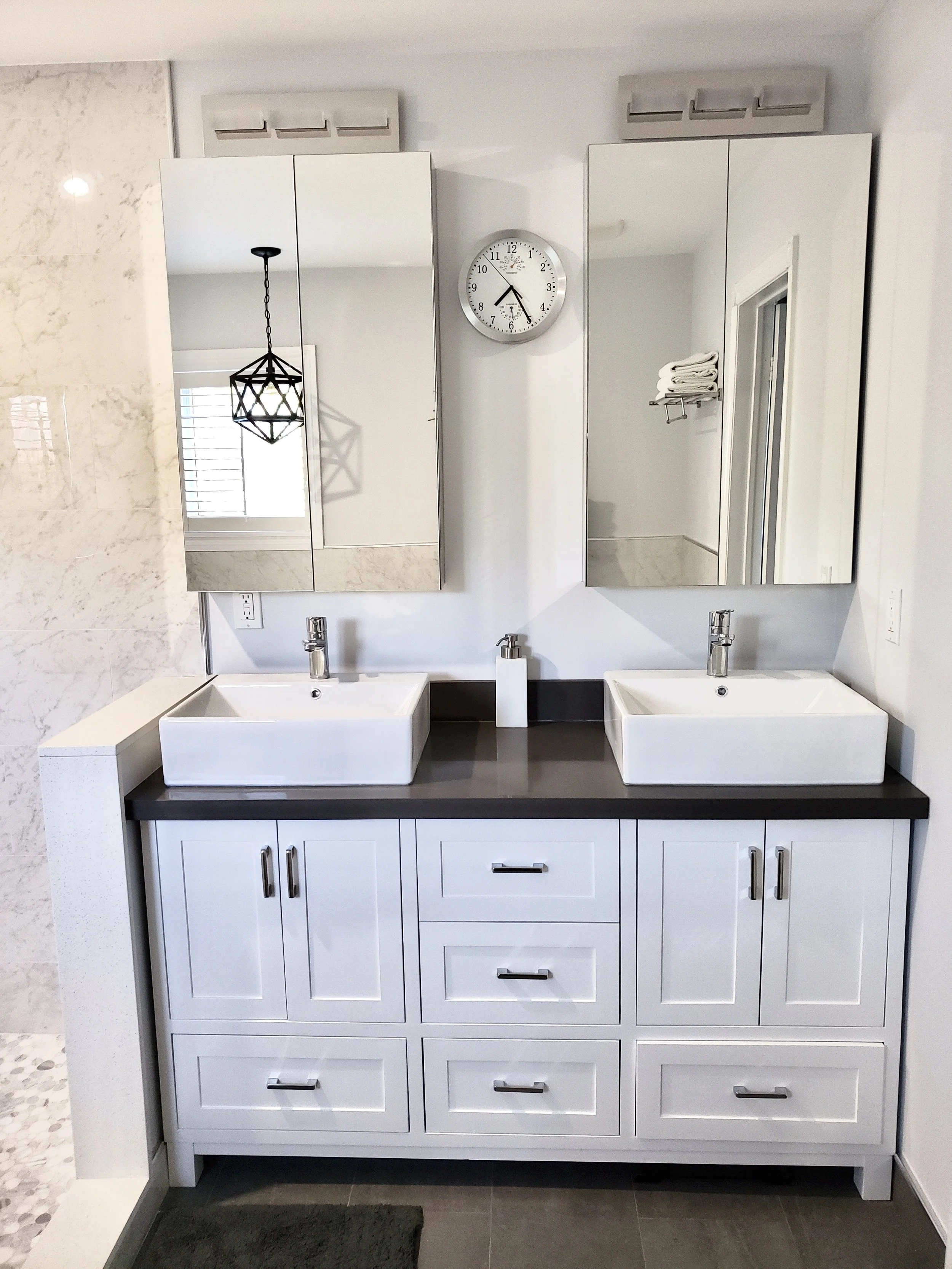 Bathroom vanity with two white vessel sinks, mirrors, and a clock above the sinks.