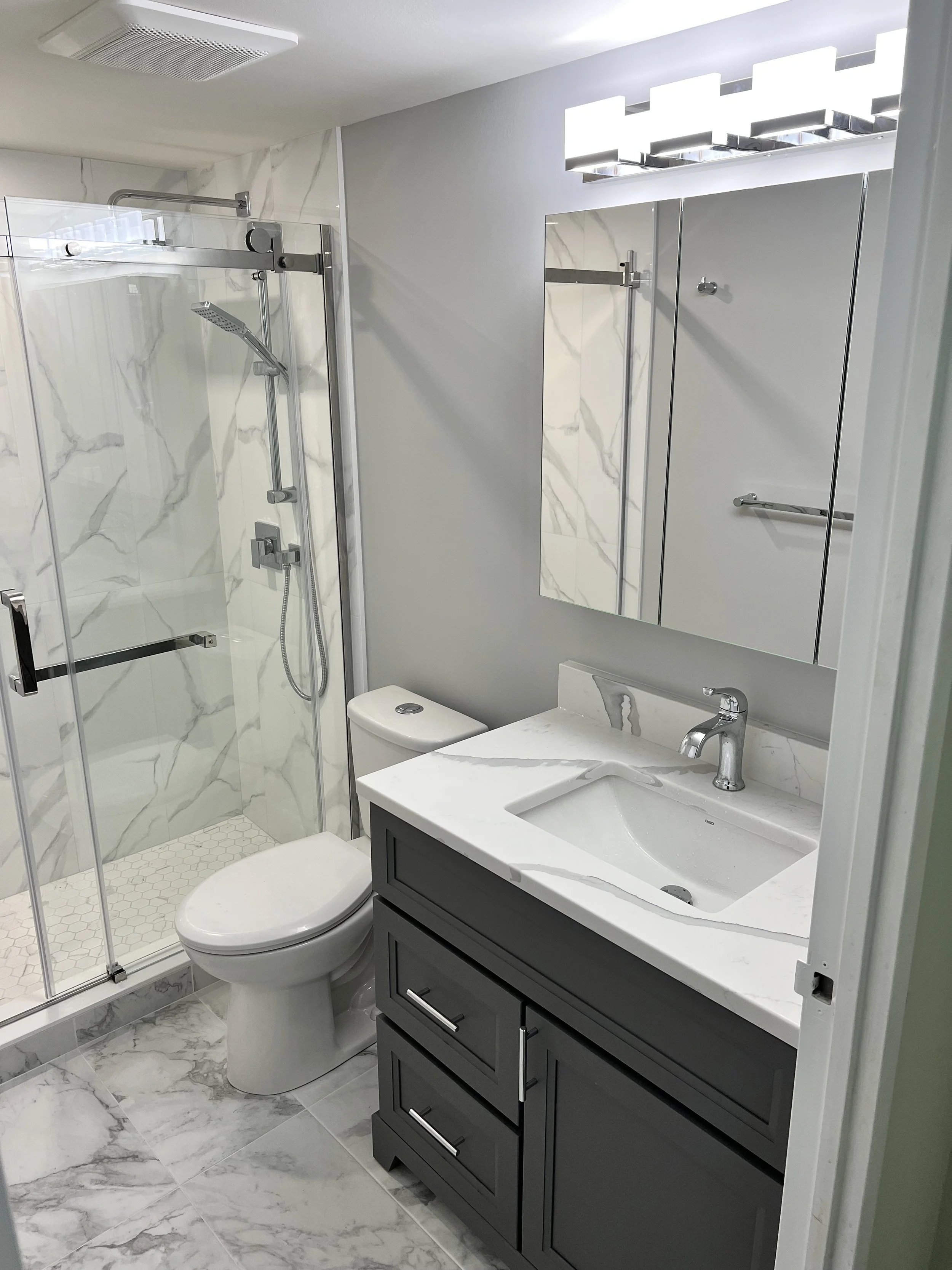 Modern bathroom with a glass-enclosed shower, a toilet, and a vanity with a marble countertop and a mirror with built-in lighting.