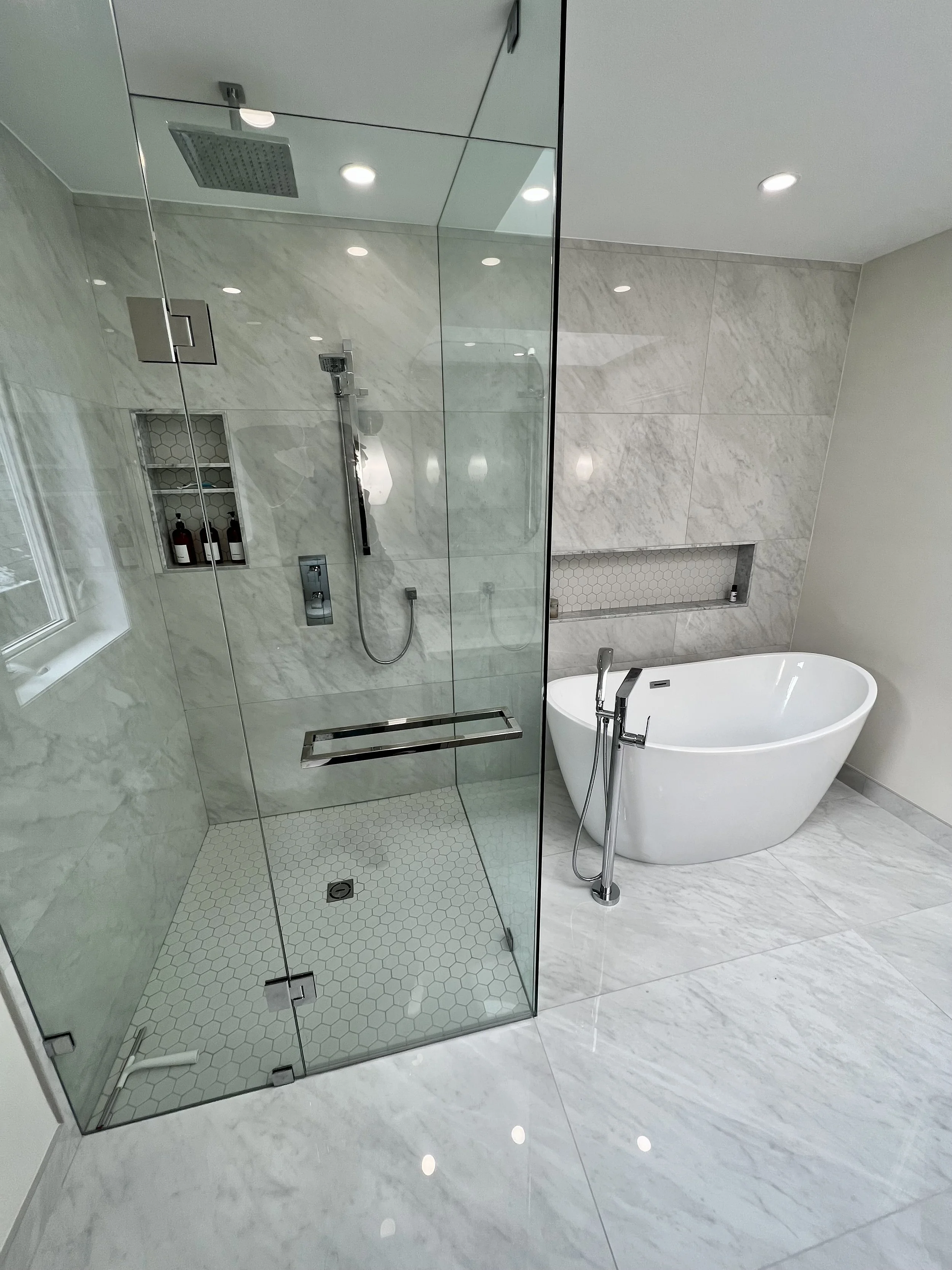 Modern bathroom with a walk-in glass shower and a freestanding bathtub, both on a marble floor.