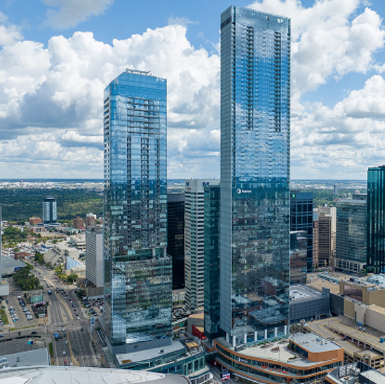 Two tall modern glass skyscrapers in a city skyline with a partly cloudy sky.
