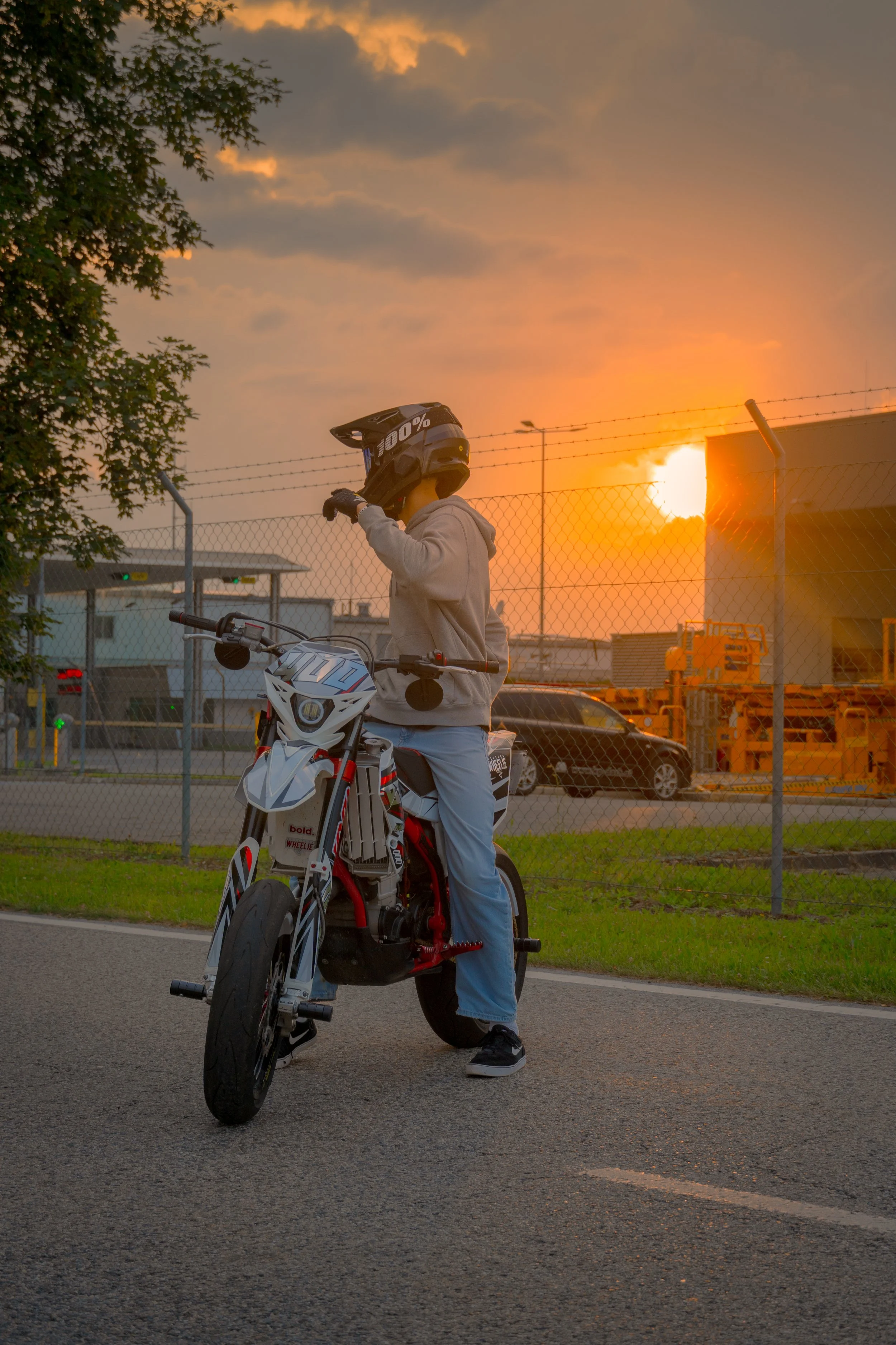 Junge Person mit Helm auf einem Elektromotorrad steht auf der Straße bei Sonnenuntergang