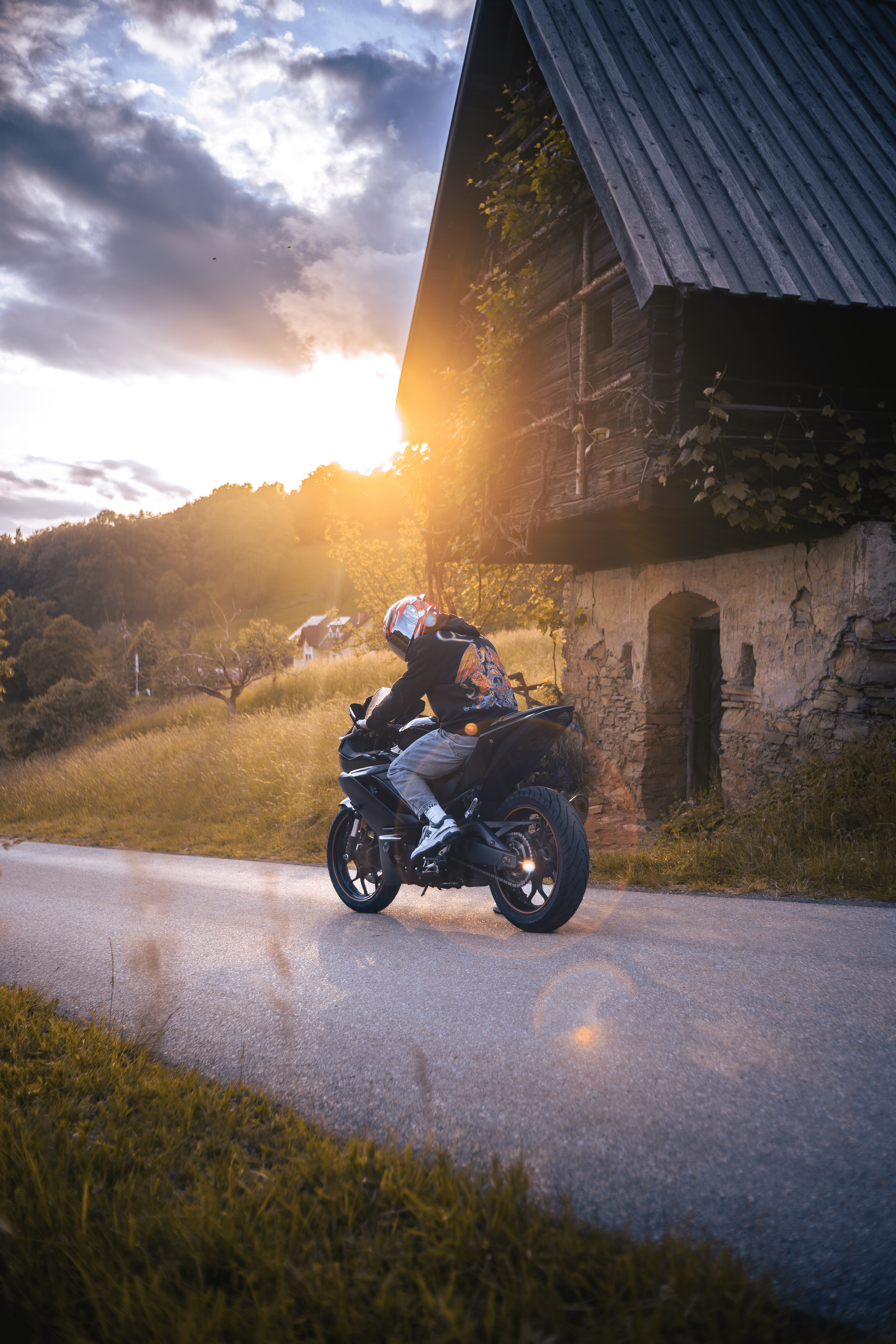 Ein Motorradfahrer fährt bei Sonnenuntergang an einer ländlichen Gegend mit alten Häusern vorbei.