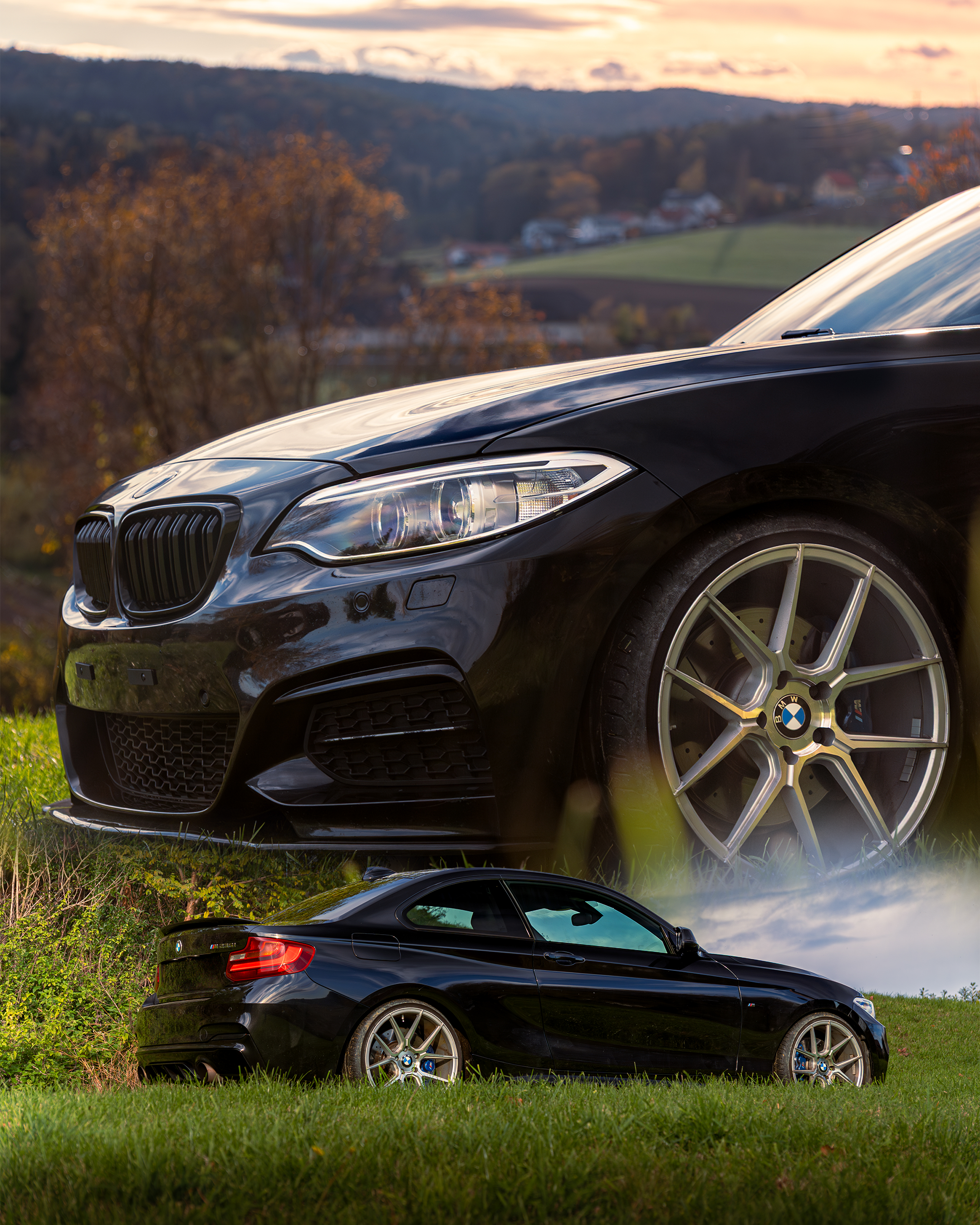 Zwei schwarze BMW-Coupes, eines im Vordergrund, das andere im Hintergrund, auf einer Wiese, mit Hügeln und Häusern im Hintergrund bei Sonnenuntergang.