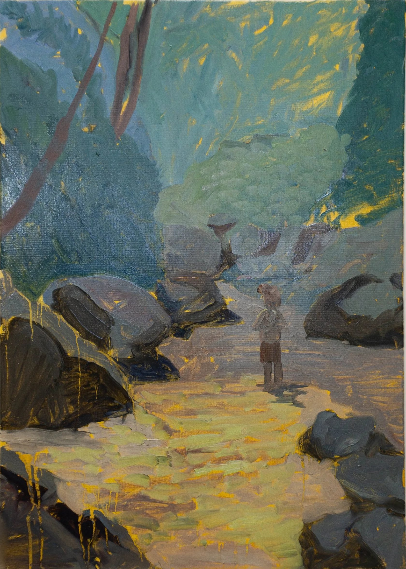 A person standing on a dirt path surrounded by large rocks and lush green trees, with sunlight filtering through the foliage.