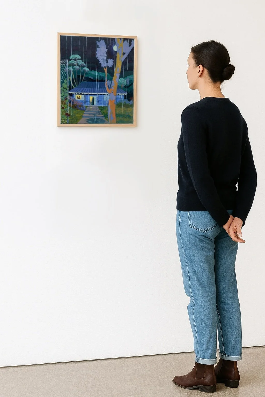 A woman in jeans and a black sweater stands in front of a painting of a rain-forest scene at an art gallery.