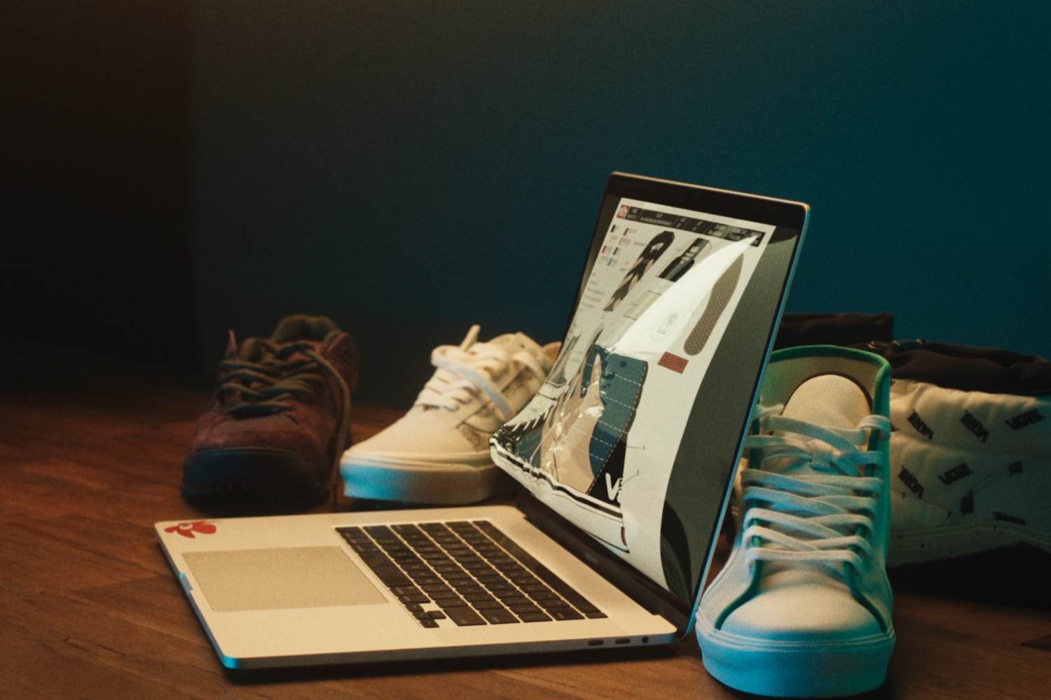 A damaged laptop with a broken screen, two pairs of sneakers on a wooden surface, and a shoe bag in the background.