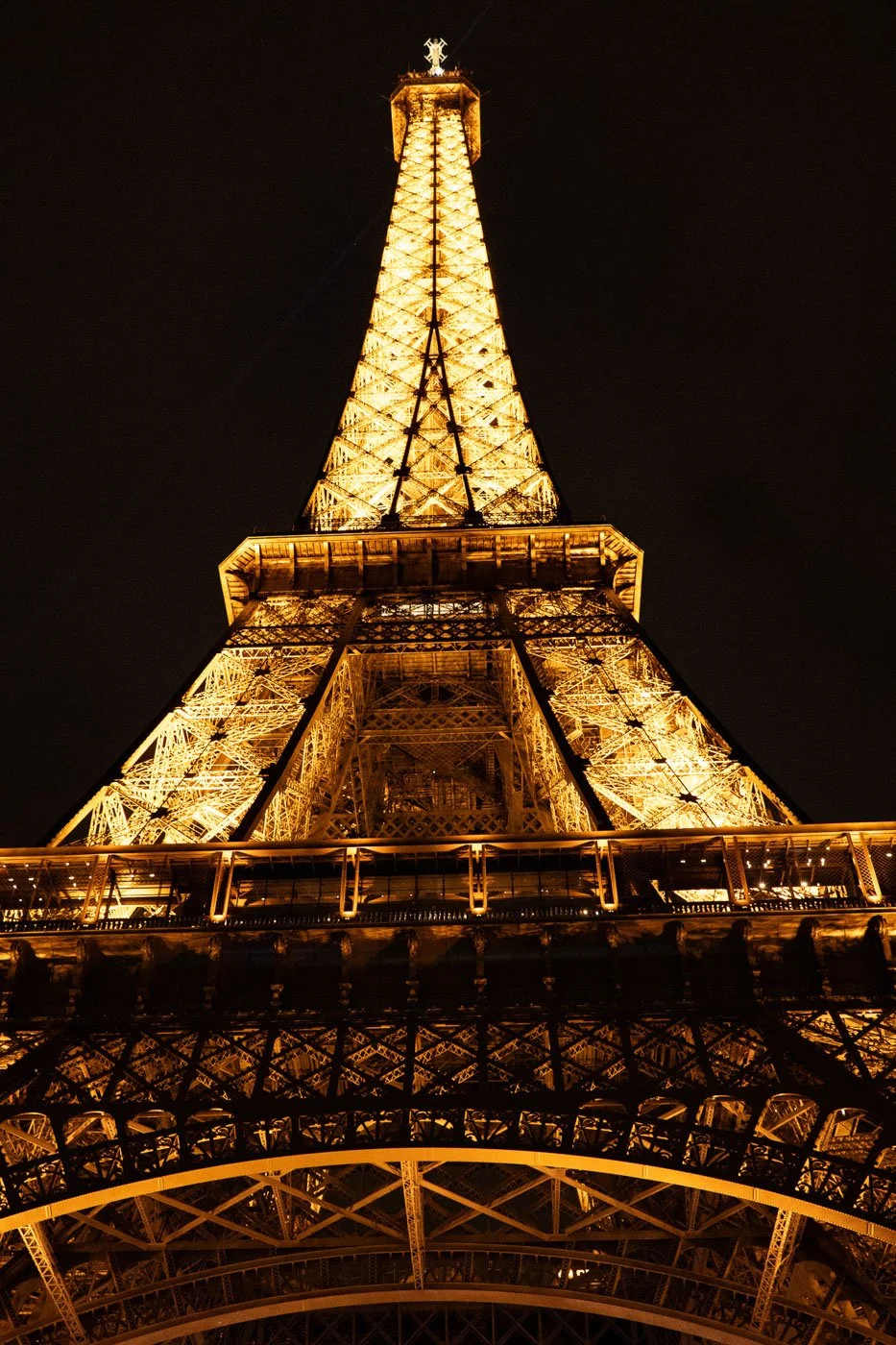 The illuminated Eiffel Tower rising vertically from a low angle against the night sky in Paris, France.