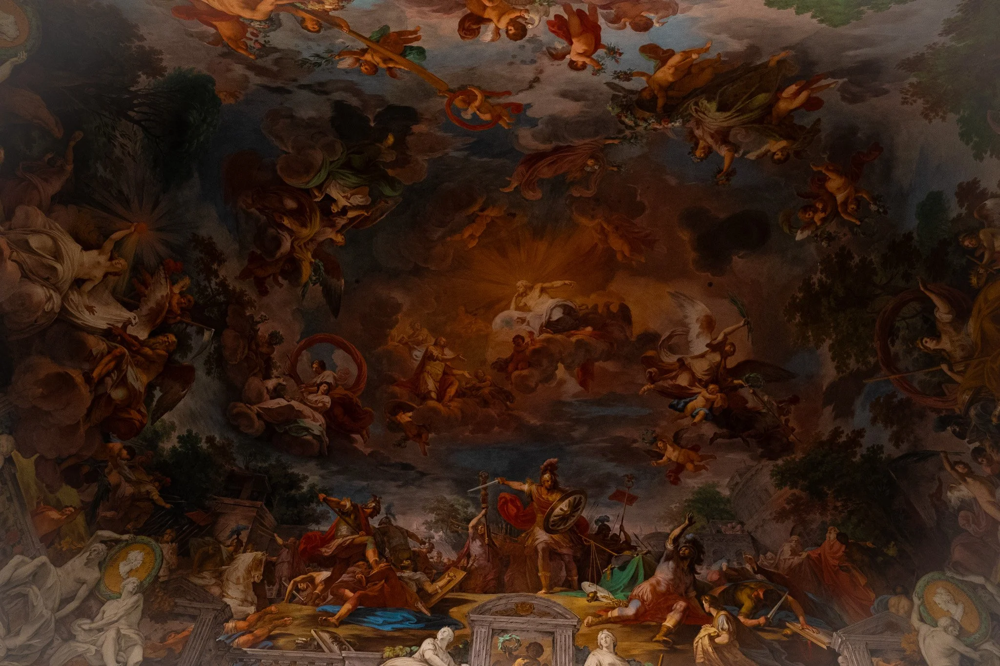 Dramatic Baroque ceiling fresco in Rome, Italy, depicting mythological figures and clouds with glowing central light in an ornate interior.