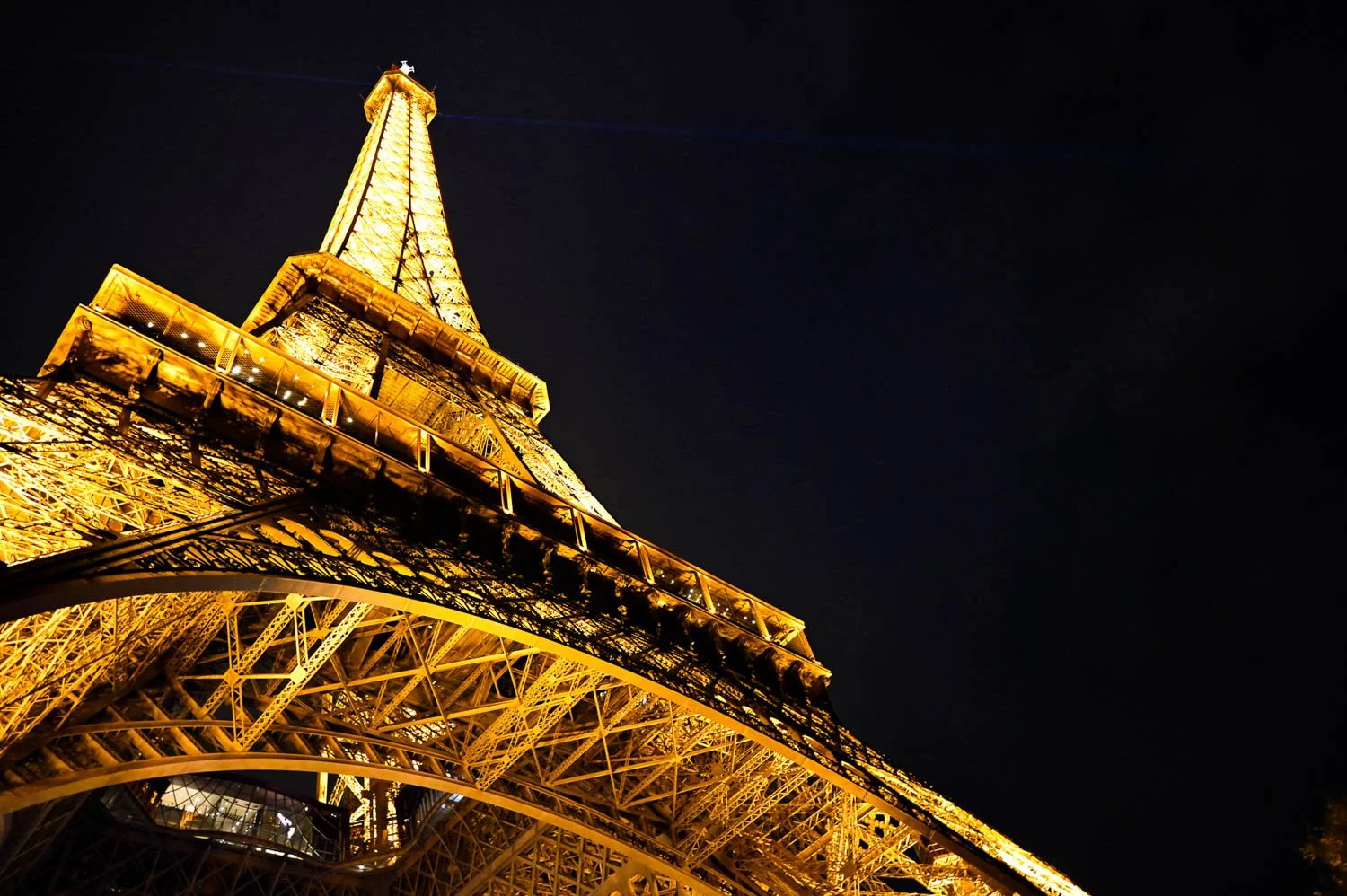 A diagonal upward view of the illuminated Eiffel Tower against a dark night sky in Paris, France.