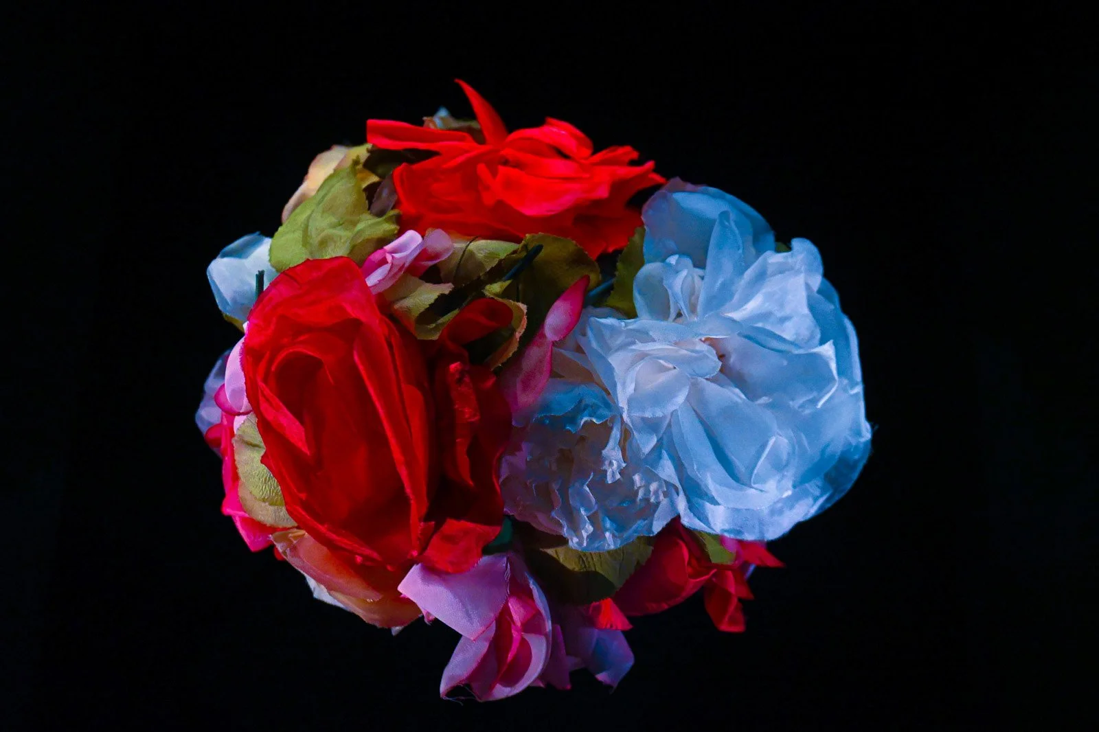 Illuminated floral installation featuring layered red, pink, and blue fabric flowers displayed at La Galerie Dior in Paris, France.