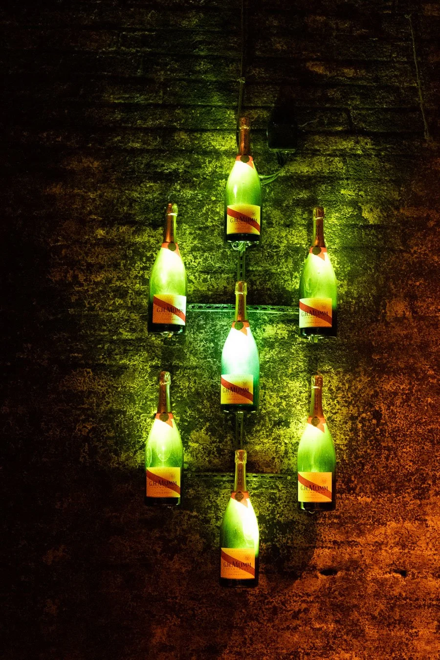 Seven G.H. Mumm wine bottles arranged as a decorative light display on the wall inside the underground cellars in Reims, France.