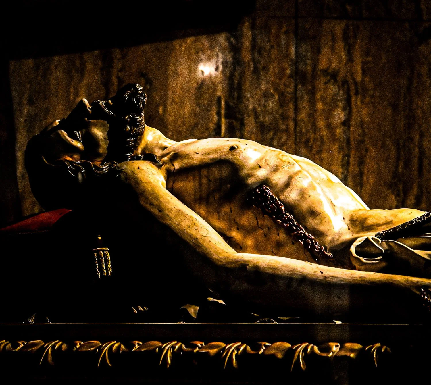Dramatically lit baroque sculpture of Christ inside an Italian church or museum, emphasizing the sculpted torso, expressive posture, and textured stone surface.