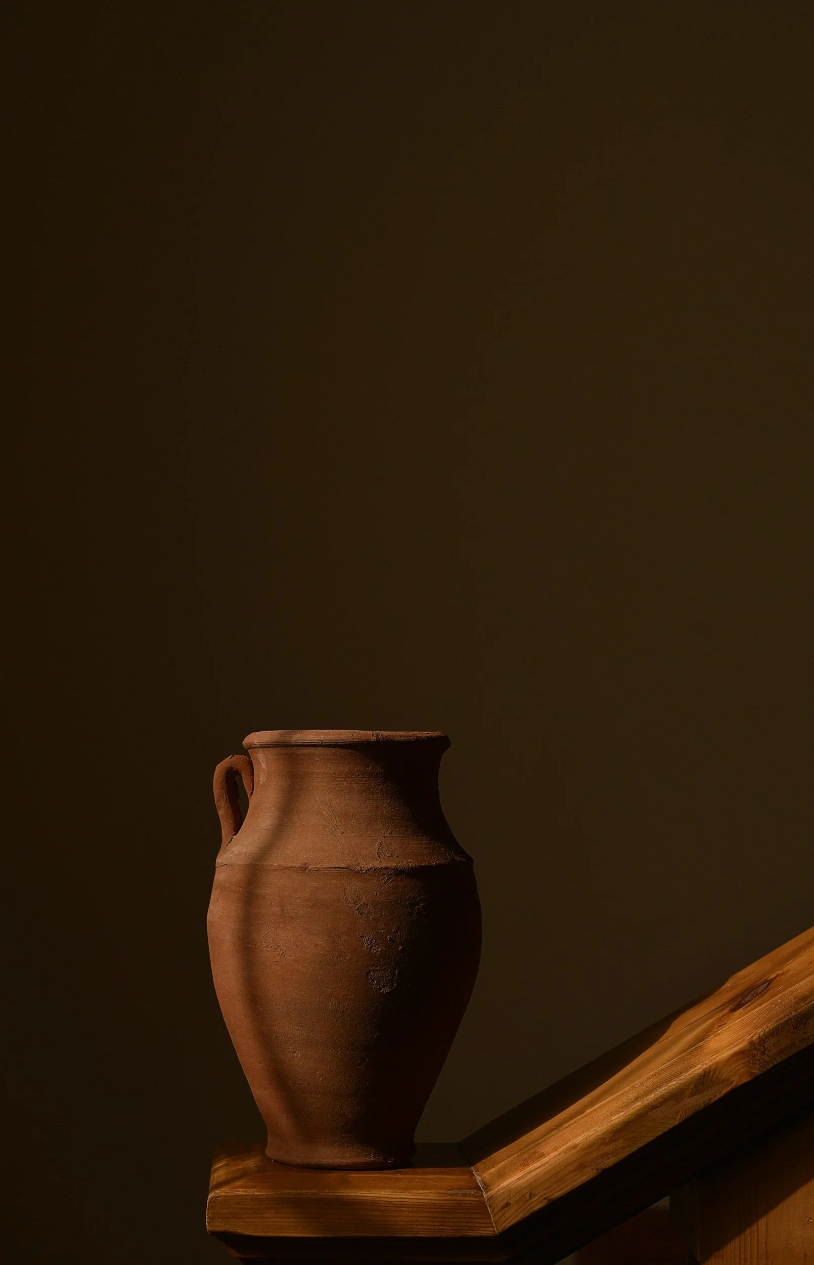 A brown clay pot with a small handle on a wooden surface against a dark background.