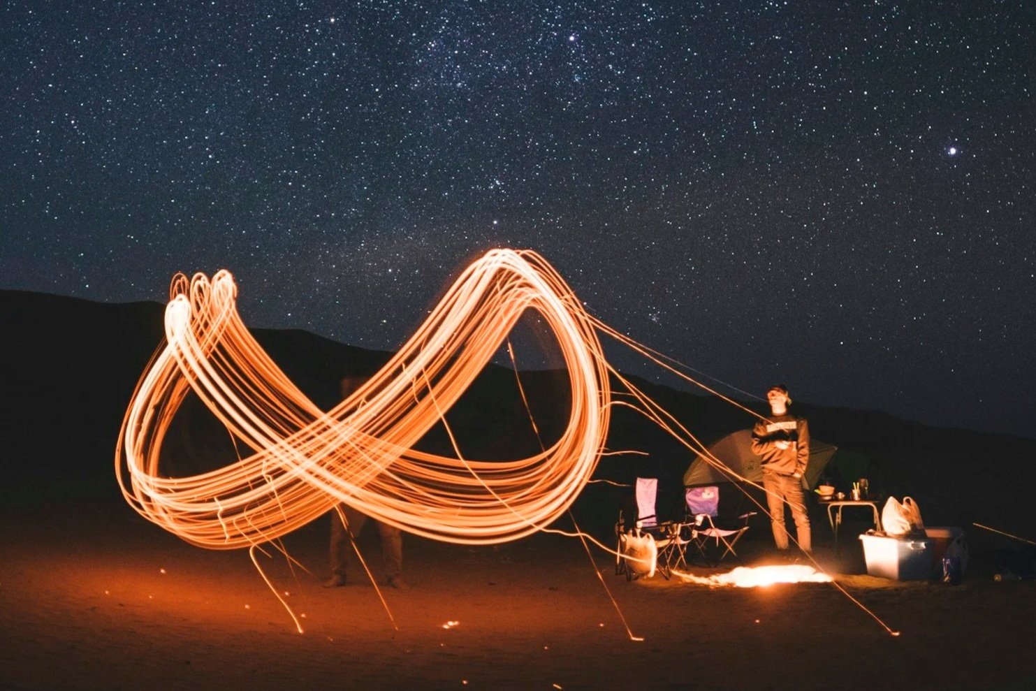 Outside scene at night, with a figure creating the illusion of a gold infinity symbol (the autism logo) out of something made of light, like a sparkler