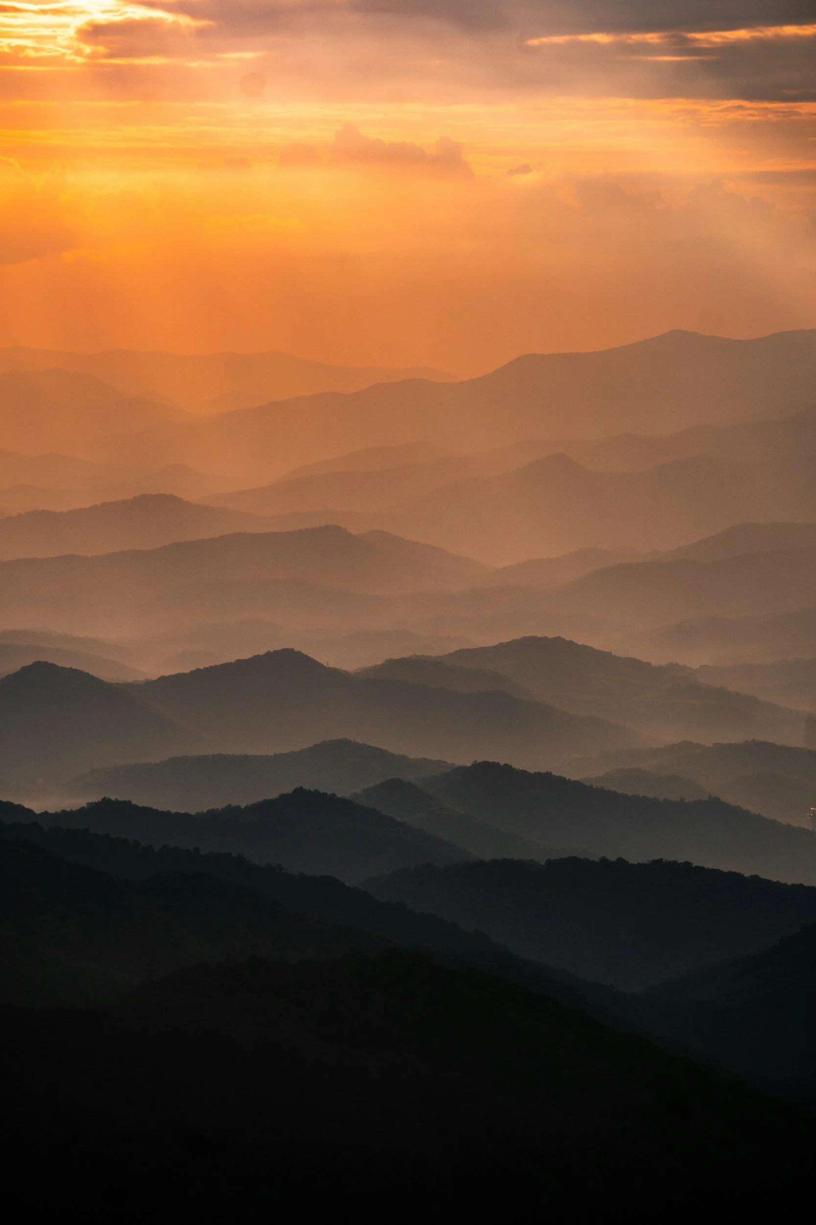 Sunset over layered rolling mountains with orange and pink sky.