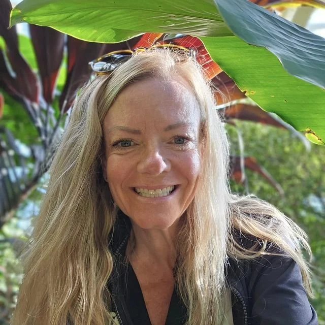 en leaves, smiling at the camera, with sunlight highlighting her blonde hair.