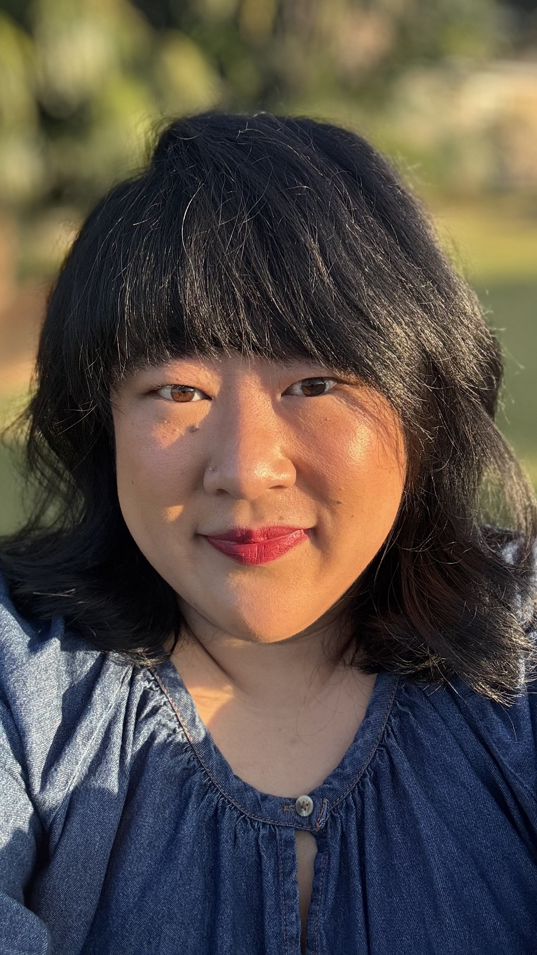 A woman (Claire) with black hair smiling outdoors during golden hour, wearing a denim top.