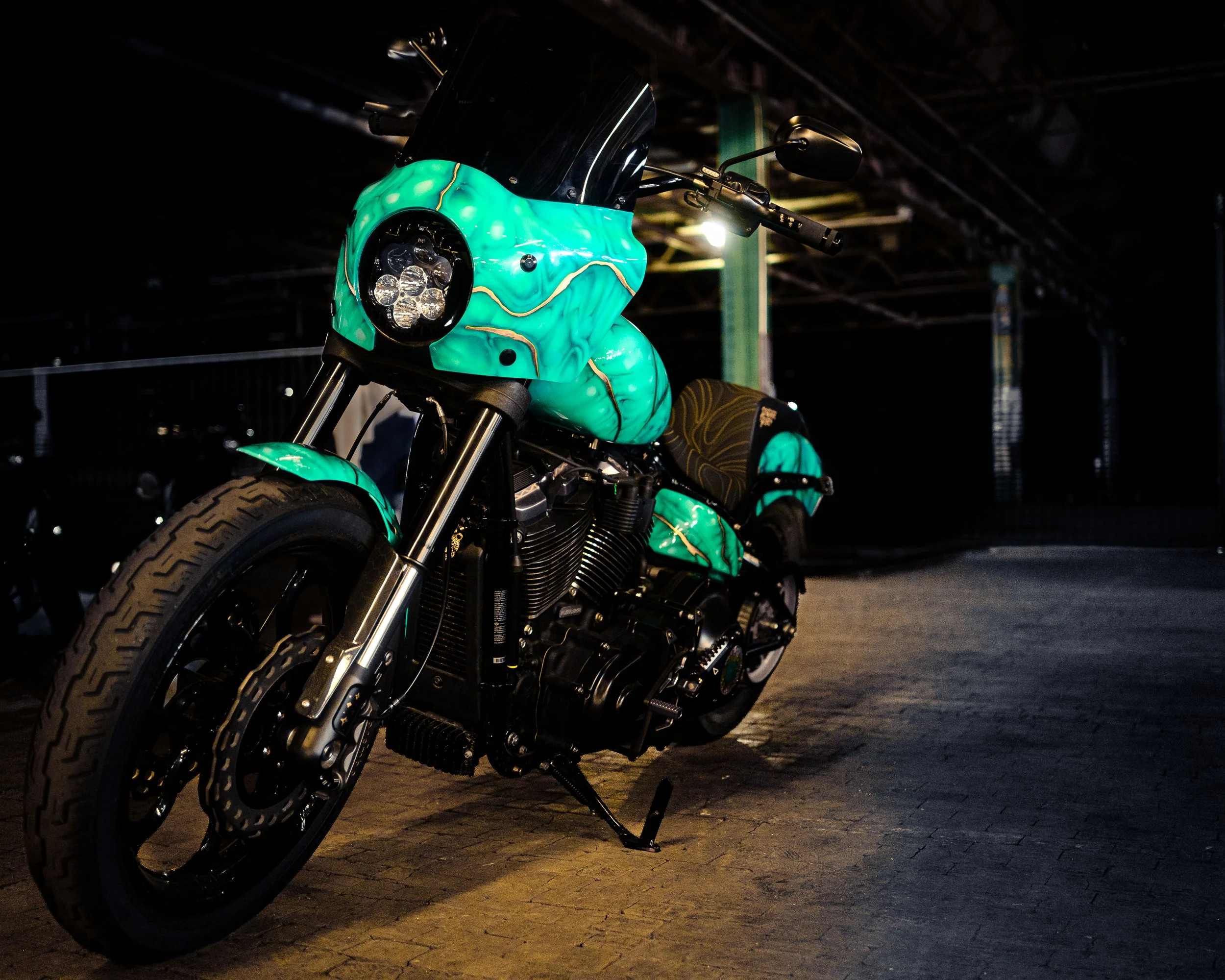 A motorcycle with turquoise and black custom paint, parked in a dimly lit indoor parking garage.
