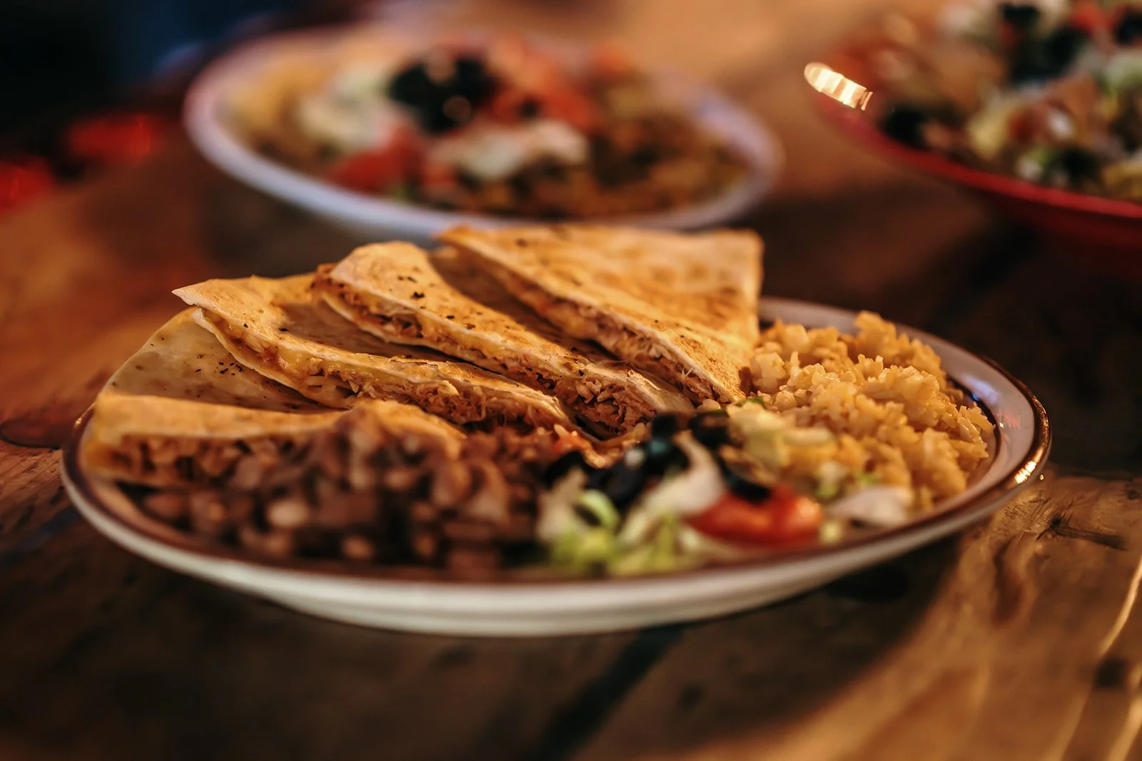 Plate with quesadillas, rice, and salad on a rustic wooden table.
