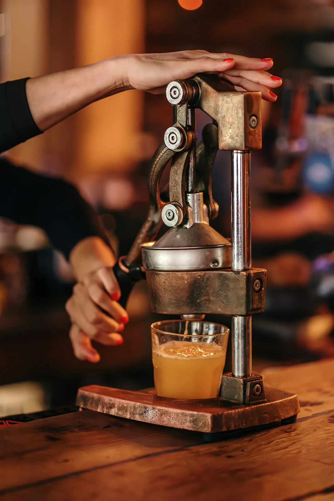 A person using a vintage manual citrus juicer to extract juice into a glass on a wooden table.