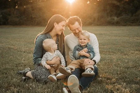A family of four sitting on the grass during golden hour, smiling and enjoying each other's company.