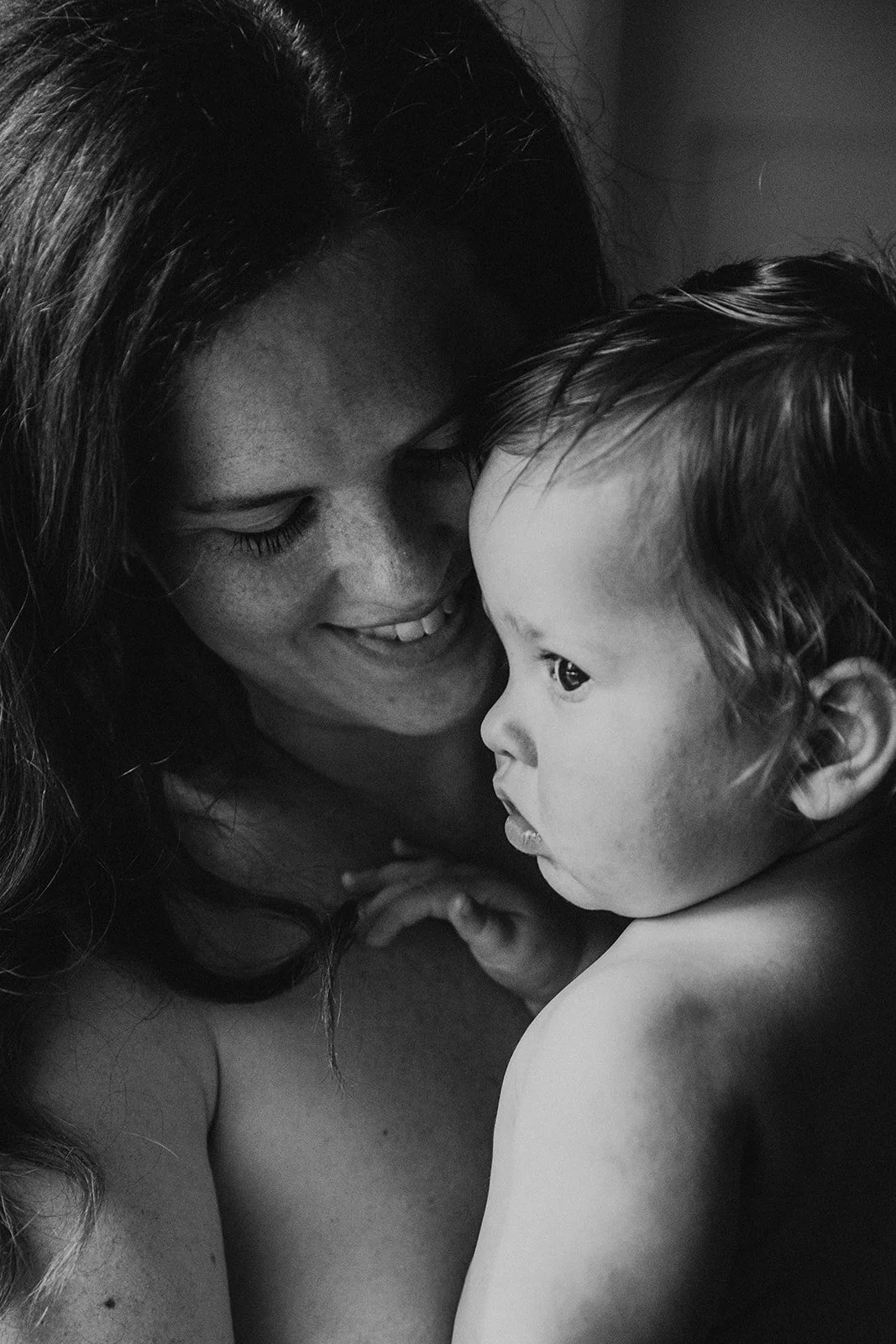 A woman and a child looking at each other closely, with the woman smiling and the child's profile visible in black and white.