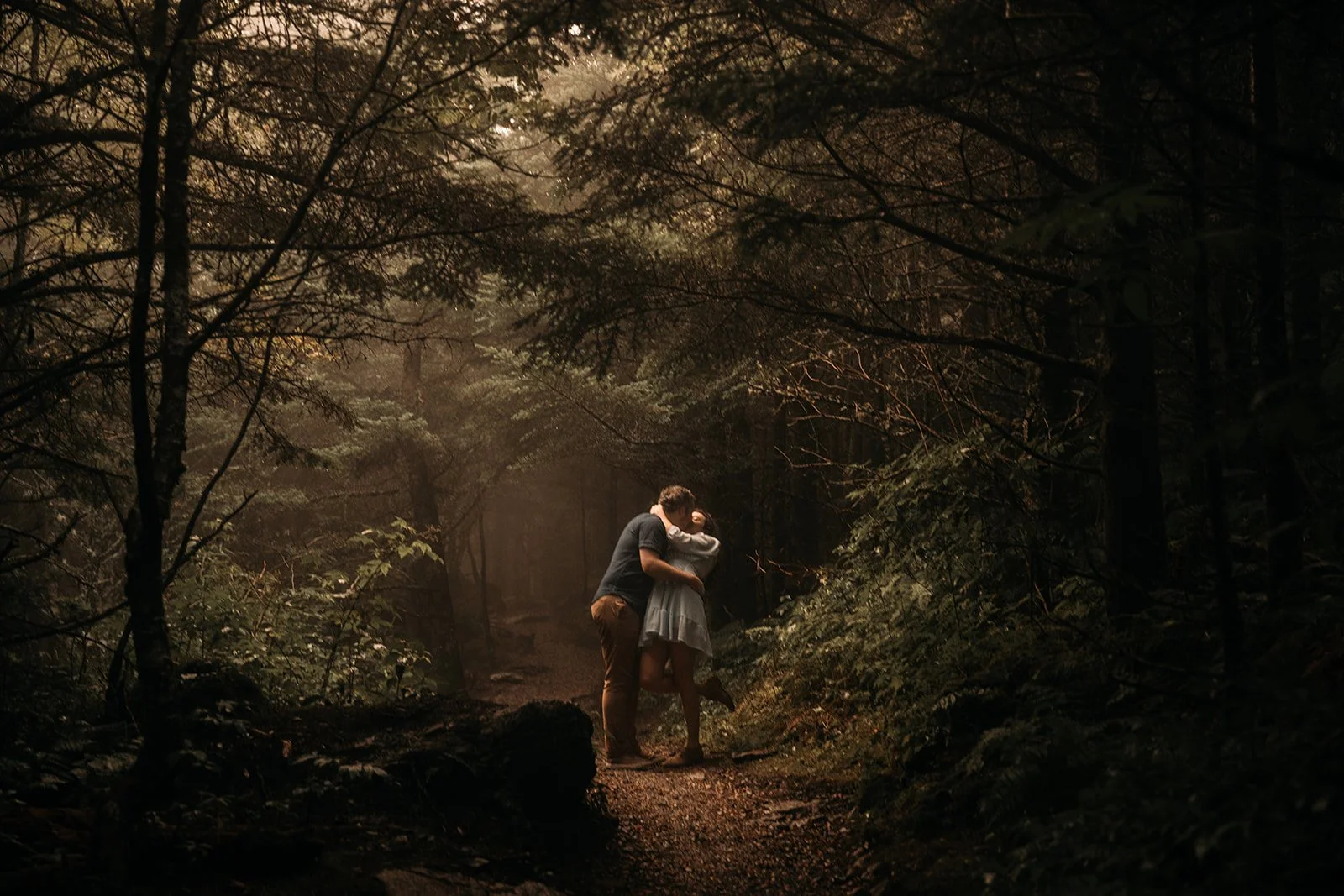 A couple sharing a kiss in a dense, wooded forest during daytime.