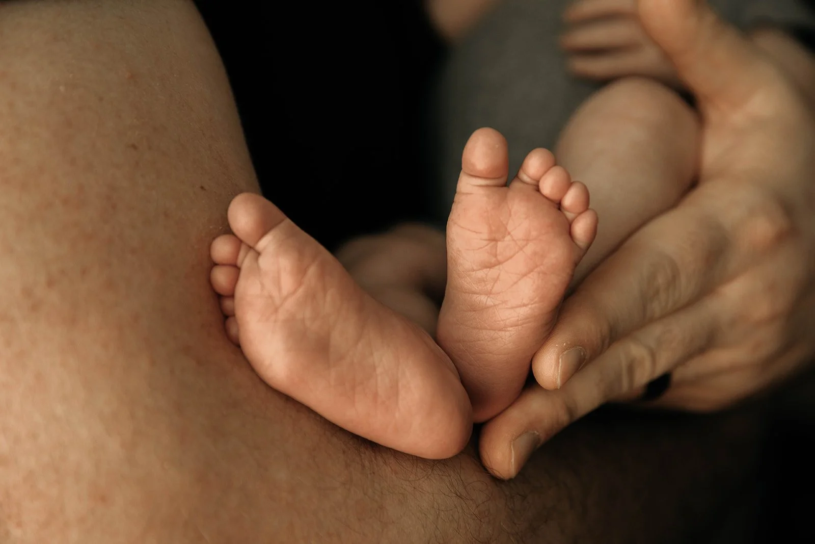 Close-up of a tiny baby's foot being held gently by an adult's hand.
