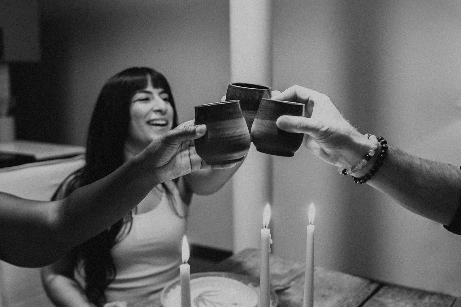 A group of people raising ceramic cups in a toast at a celebration, with a girl smiling at the birthday cake with lit candles in front of her.