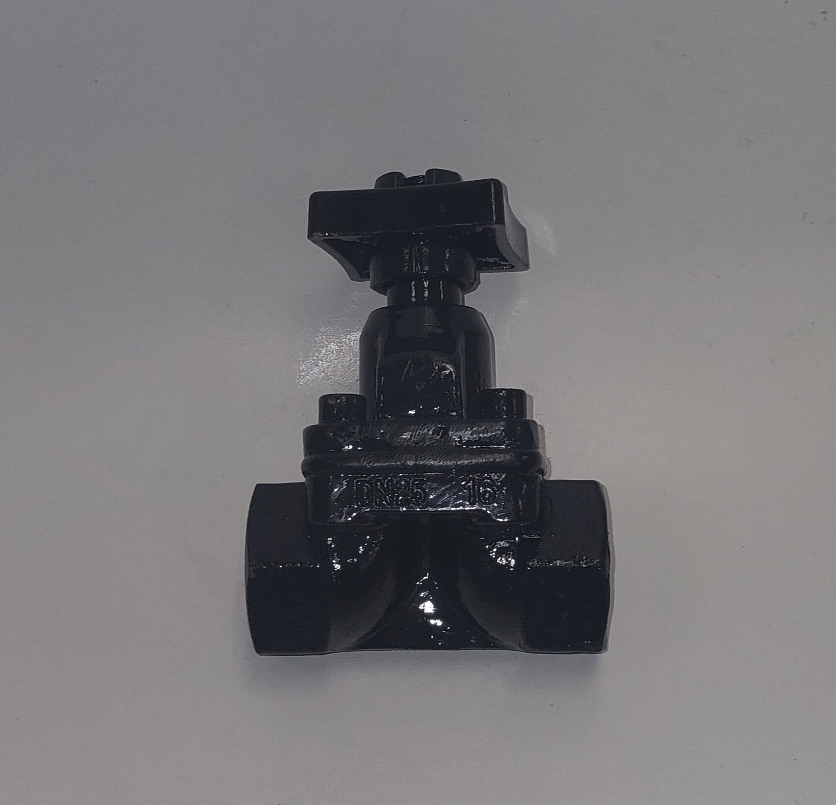 A black valve with a square head, cylindrical stem, and a rounded end on a white surface.