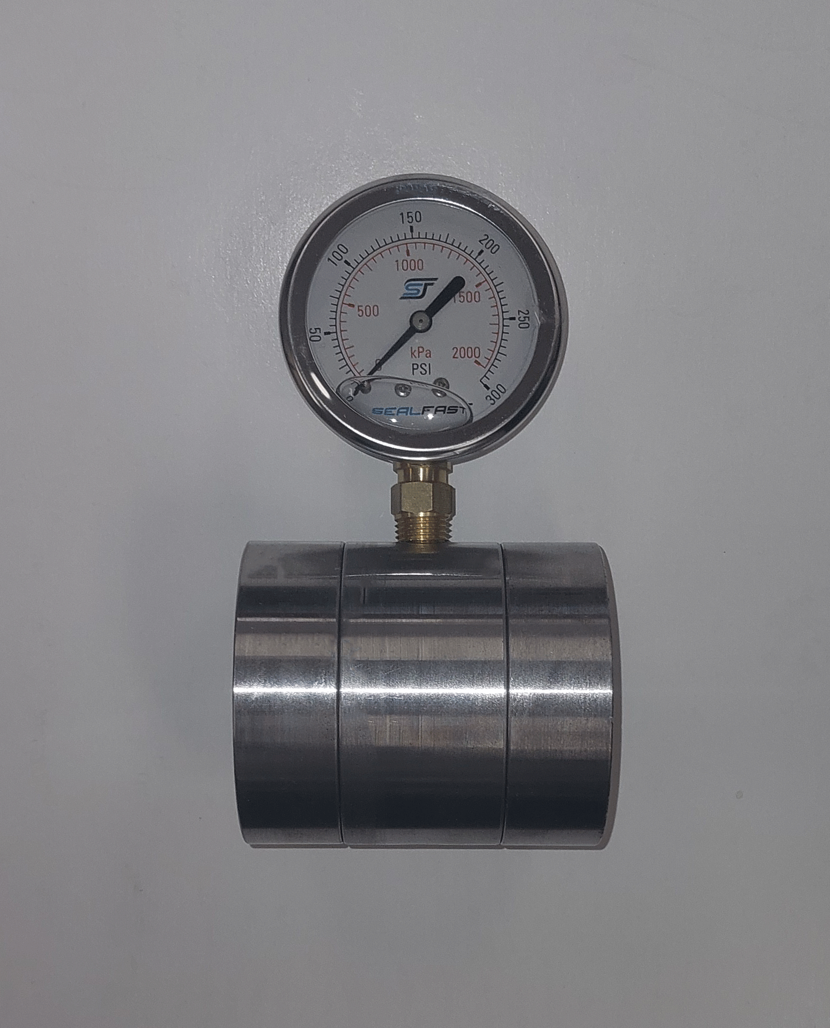 A pressure gauge connected to a metal cylinder, showing pressure readings in PSI and kPa on a white background.