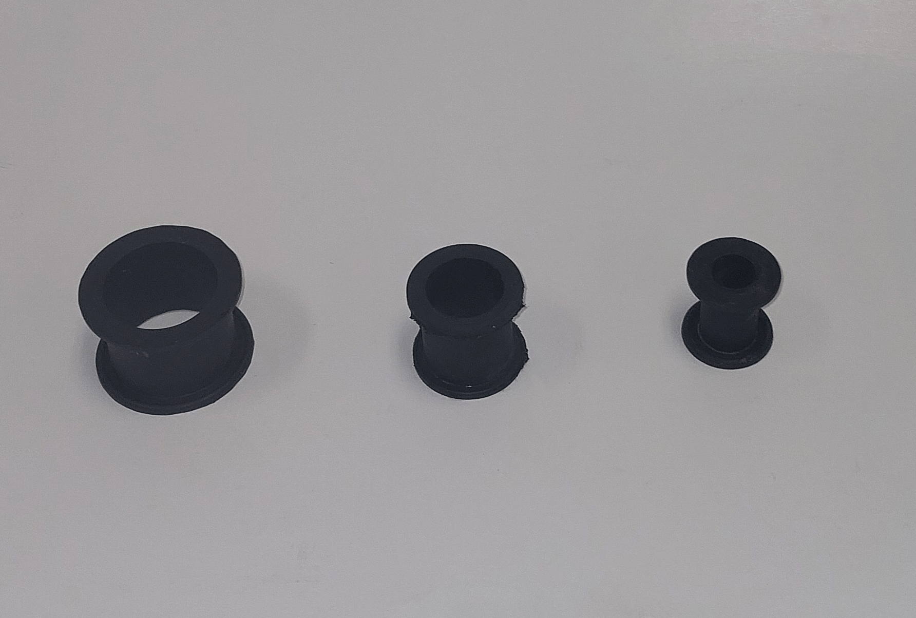 Three black rubber bushings of varying sizes placed on a white surface, arranged from largest to smallest.