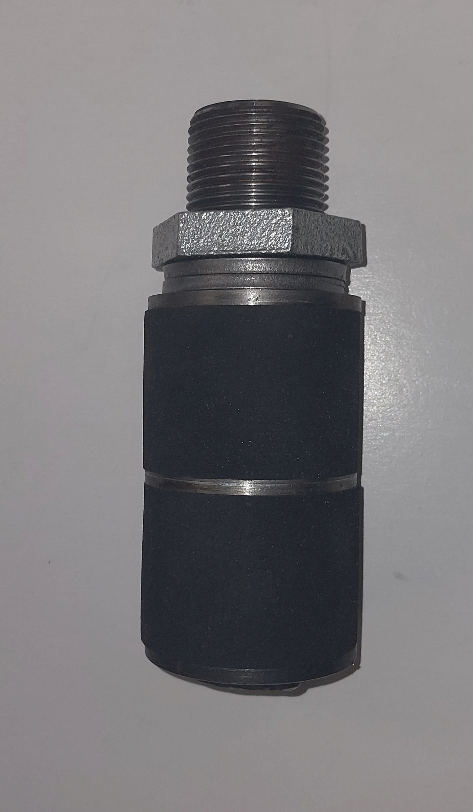A close-up of a grout packer end fitting with a threaded metal top and black cylindrical body against a plain background.