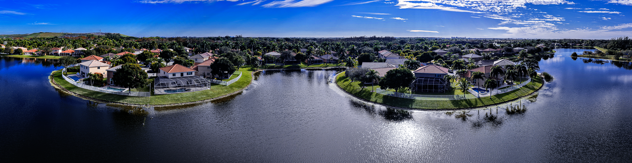 Aerial view of residential houses on small islands surrounded by water, with green lawns, trees, and clear blue sky.