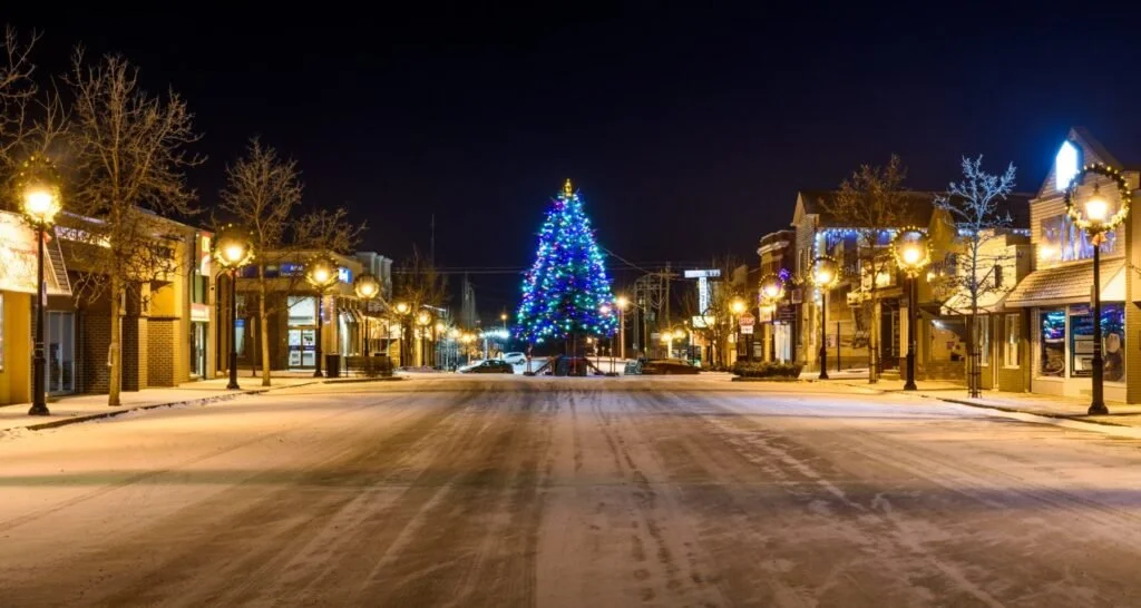 Empty street decorated for Christmas with a large, lit Christmas tree at the center and holiday lights on buildings and street lamps.