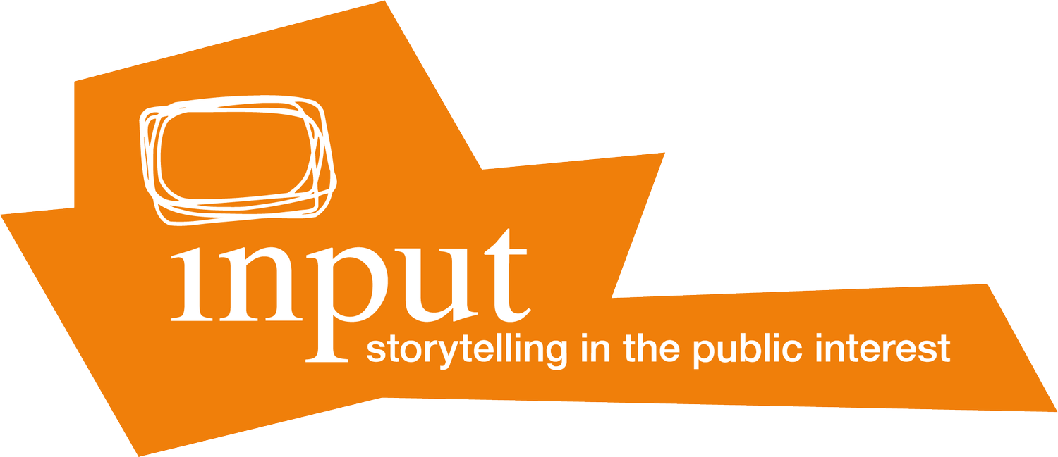 Orange abstract banner with a white outline of a rectangle and the words "input storytelling in the public interest" in white.