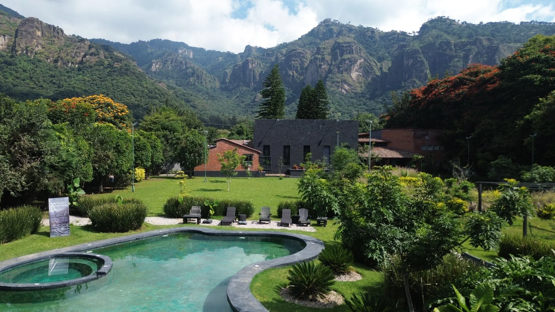 Paisaje con montaña y vegetación exuberante, alberca y sillas en un jardín