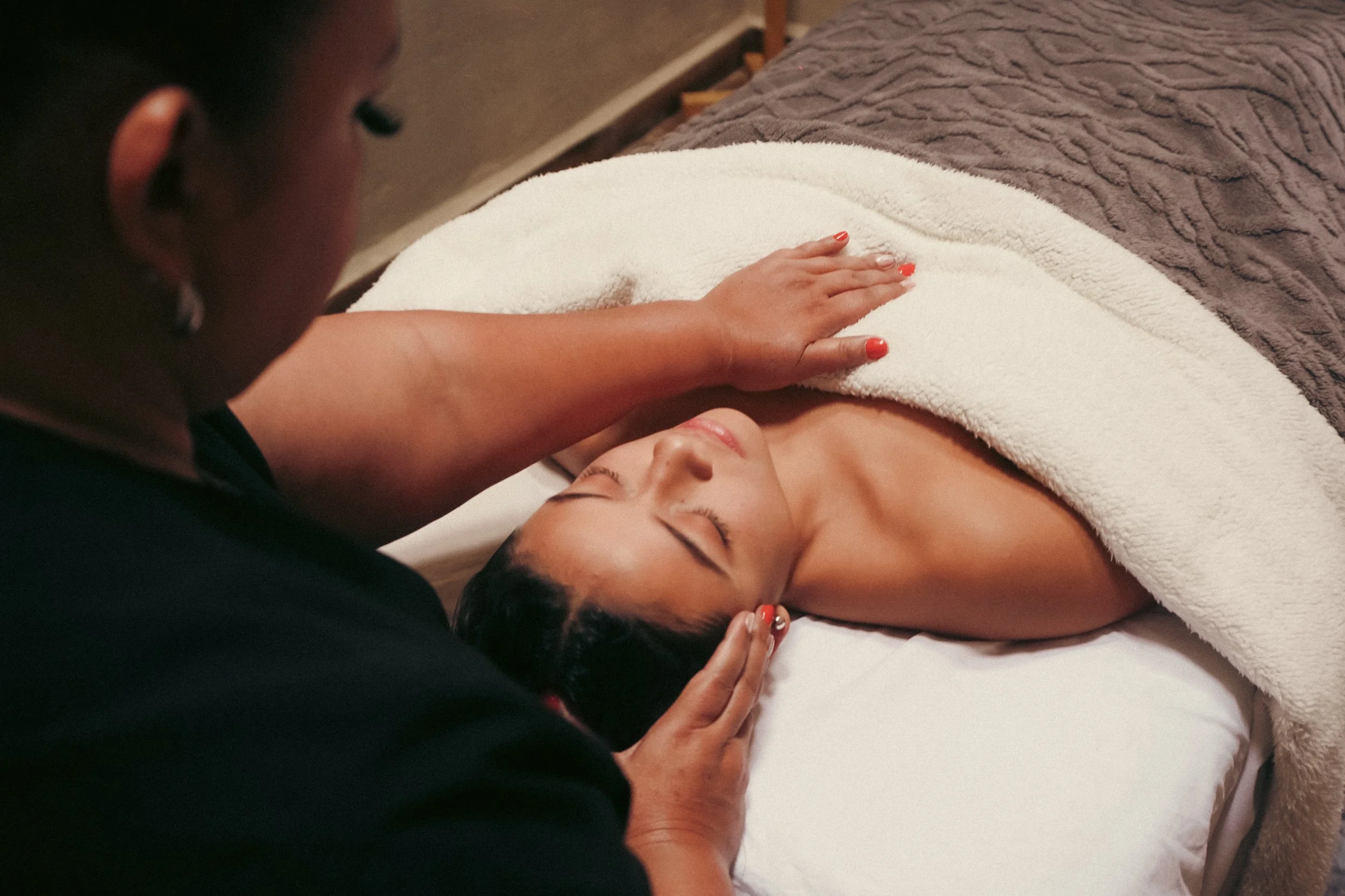 Una mujer recibiendo un masaje en la cabeza en una camilla, con una manta sobre ella.