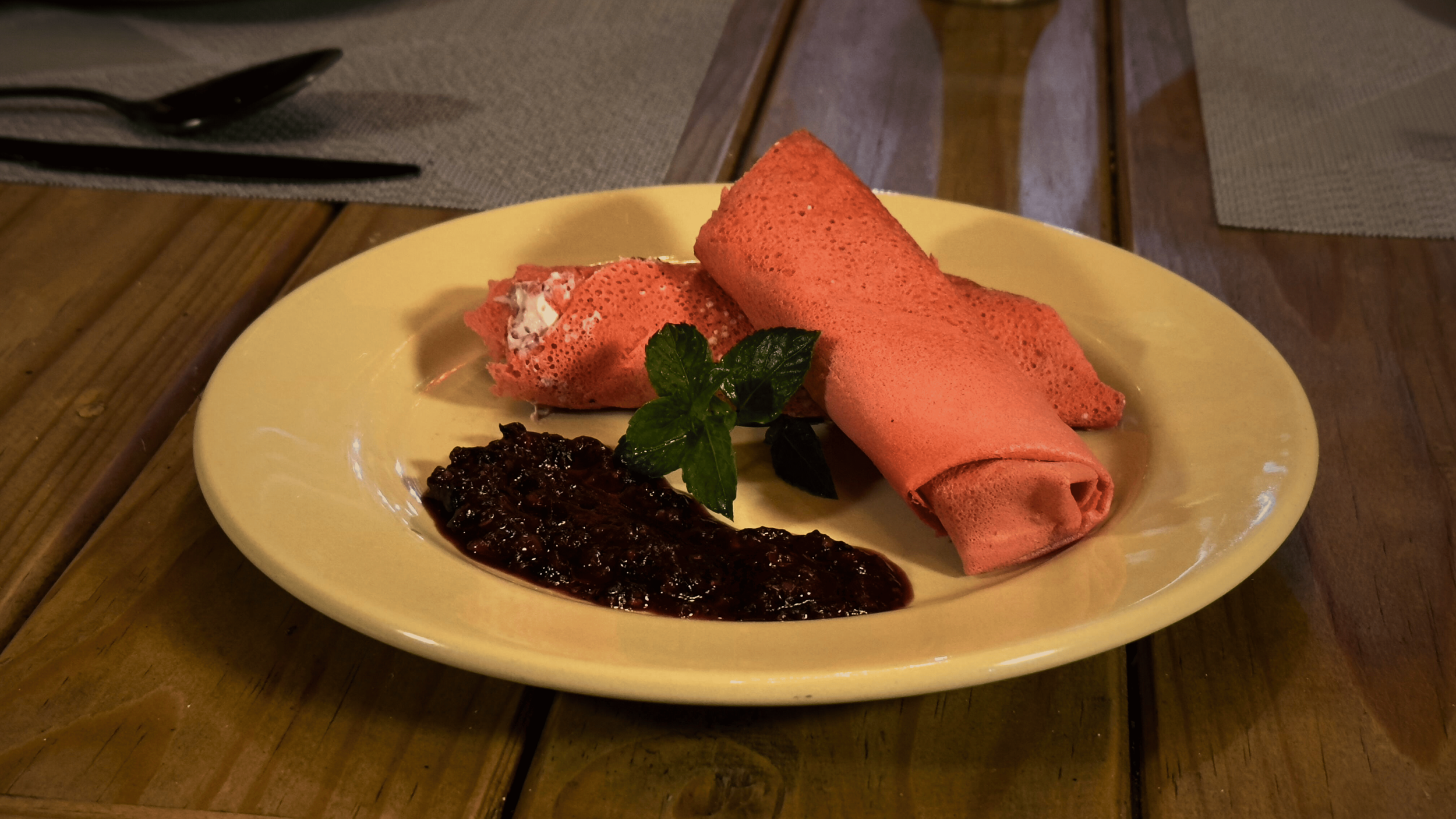 Crepes de color rosa con menta y mermelada de ciruela en un plato amarillo, en una mesa de madera.