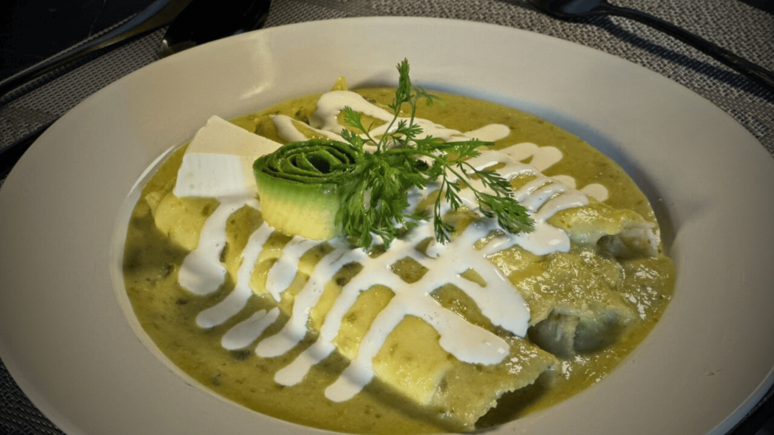 Plato de moles con pollo, adornado con crema, cilantro y rodaja de pepino en la parte superior.