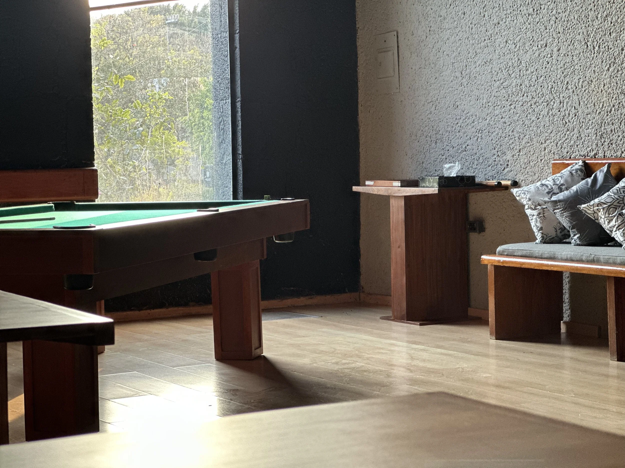 Habitación con mesa de billar, ventana con vista a árboles y sillón con cojines