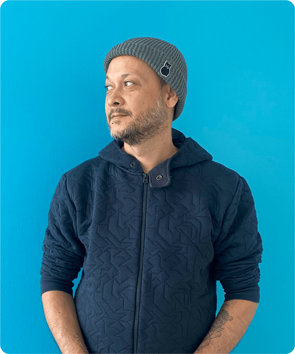 Ein Mann trägt einen grauen Strickmütze mit einem kleinen Logo und eine dunkelblaue Jacke vor einem hellblauen Hintergrund.