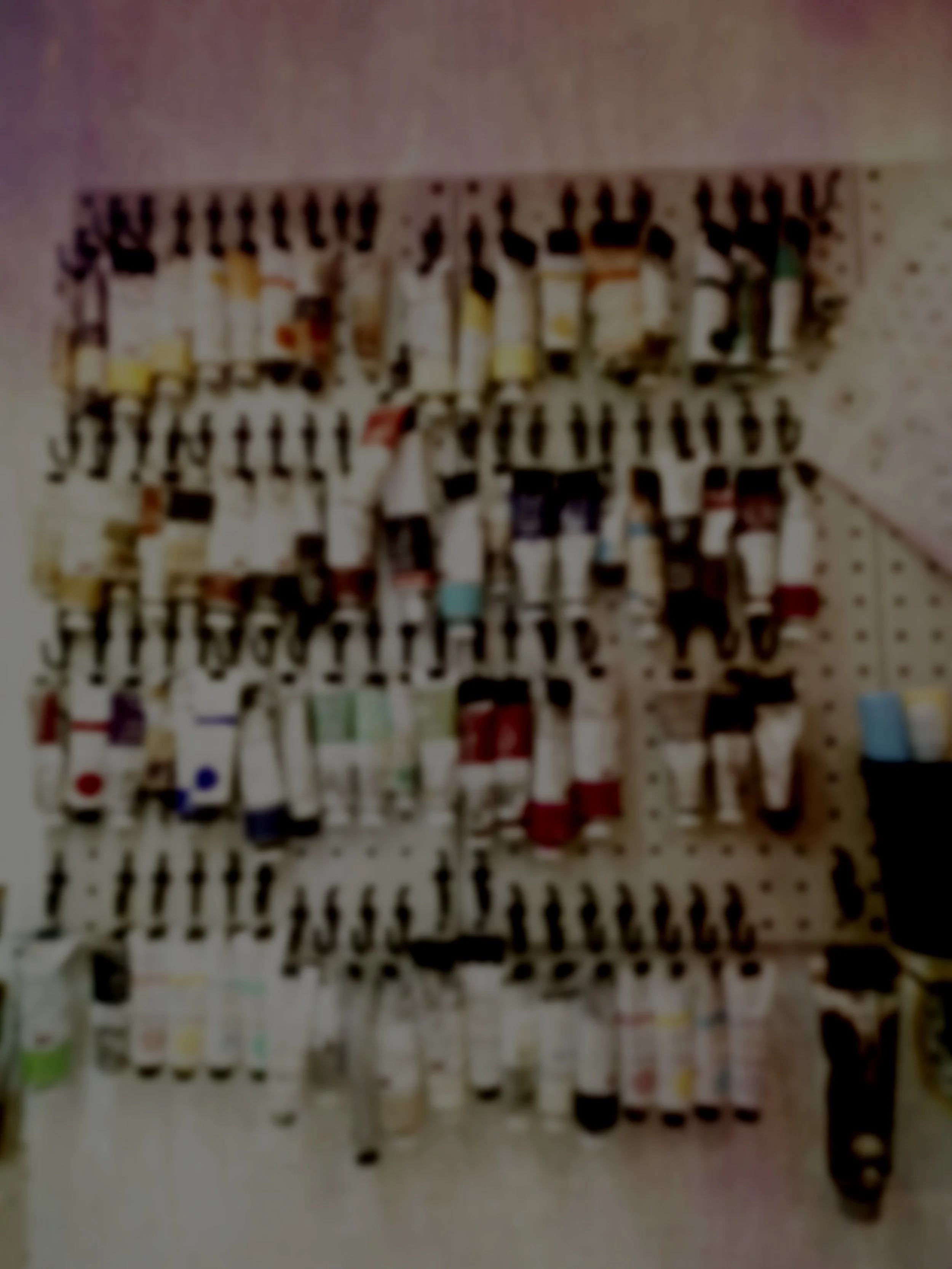 A display wall with various art supplies such as paint bottles and tubes hanging on hooks.