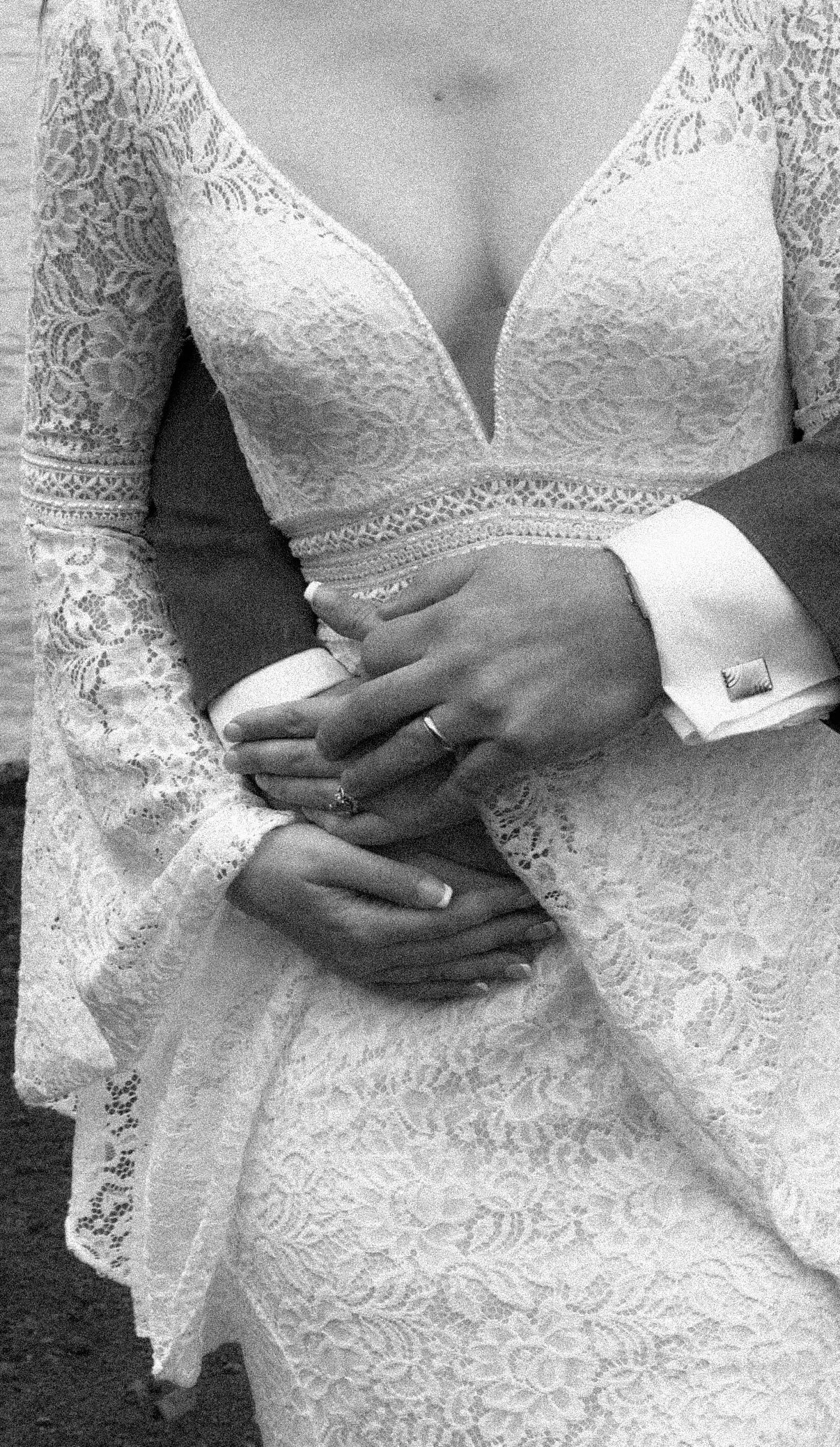 Close-up of a bride in a lace wedding dress holding hands with a groom in a suit.